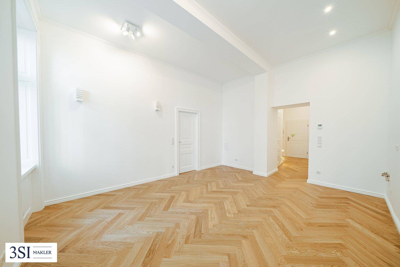 Geräumiges, leeres Wohnzimmer mit hellem Fischgrätparkett und hohen Decken, bereit zur Einrichtung.