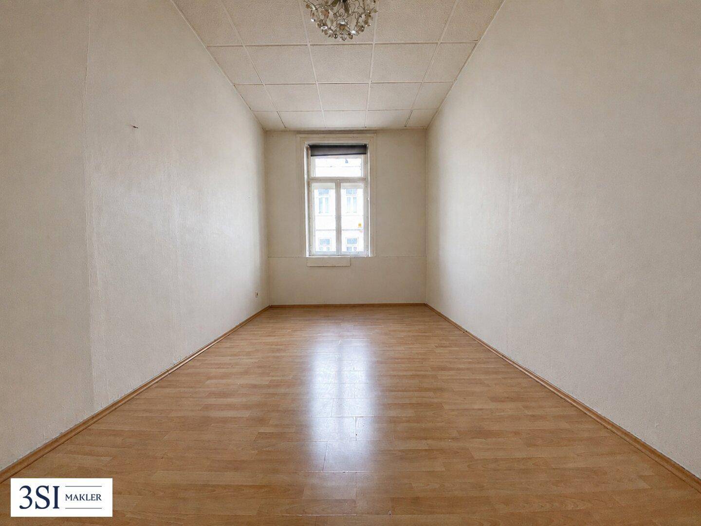 Leeres Schlafzimmer mit hellem Holzboden, hohen Decken und einem Fenster.