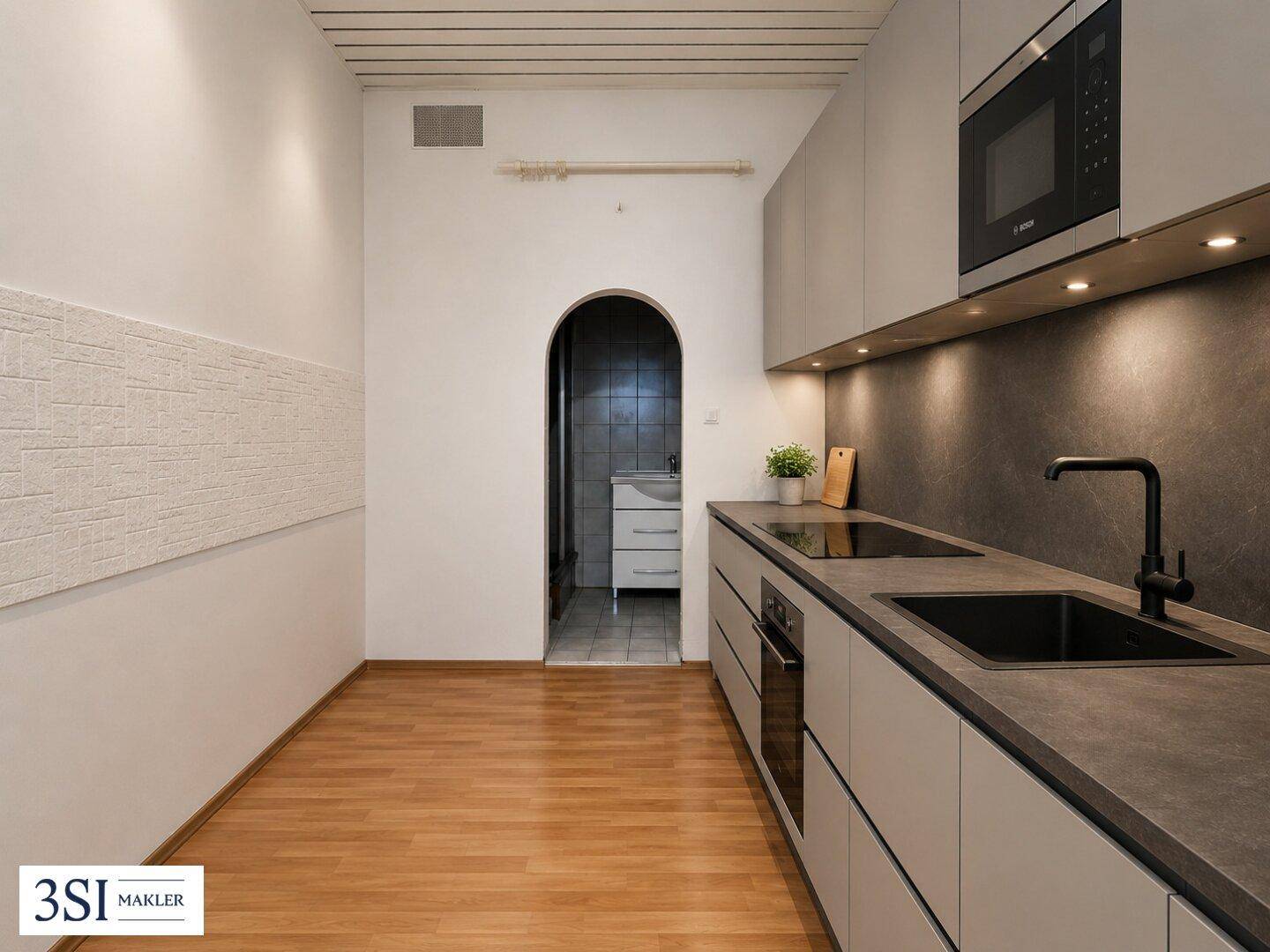 Moderne Küche mit grauen Schränken, Einbaugeräten und einem Durchgang zum Badezimmer.