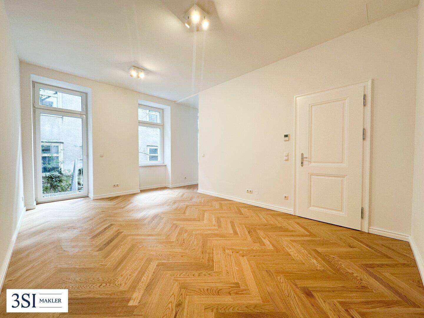 Geräumiger, heller Wohnbereich mit elegantem Fischgrätparkett und Zugang zum Außenbereich.