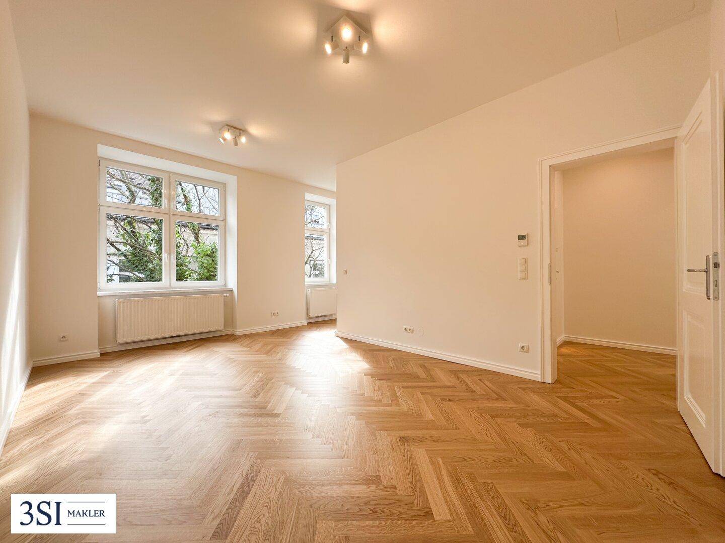 Heller Wohnraum mit klassischem Fischgrätparkett und großen Fenstern mit Blick ins Grüne.