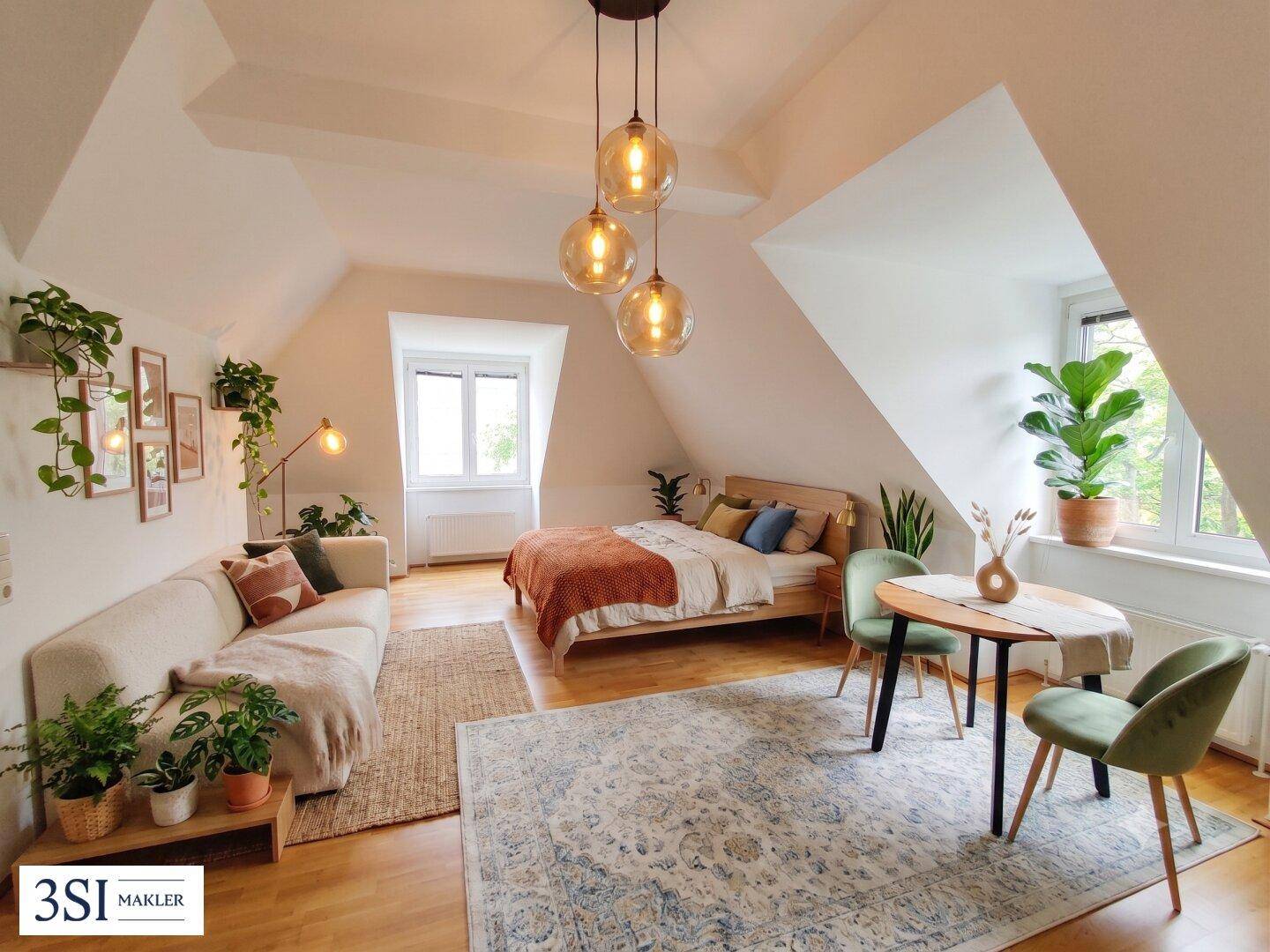 Helles Dachzimmer mit Holzboden, Bett, Sofa und Essbereich, modern eingerichtet mit vielen Pflanzen.