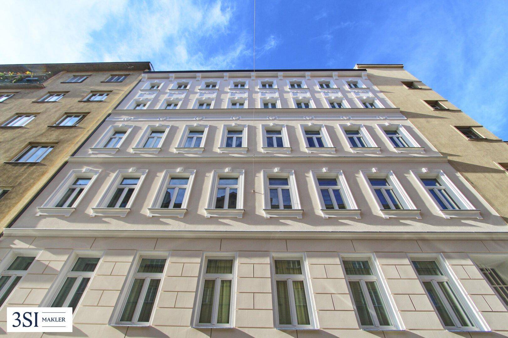 Ansicht der frisch renovierten Fassade eines Mehrfamilienhauses unter blauem Himmel.