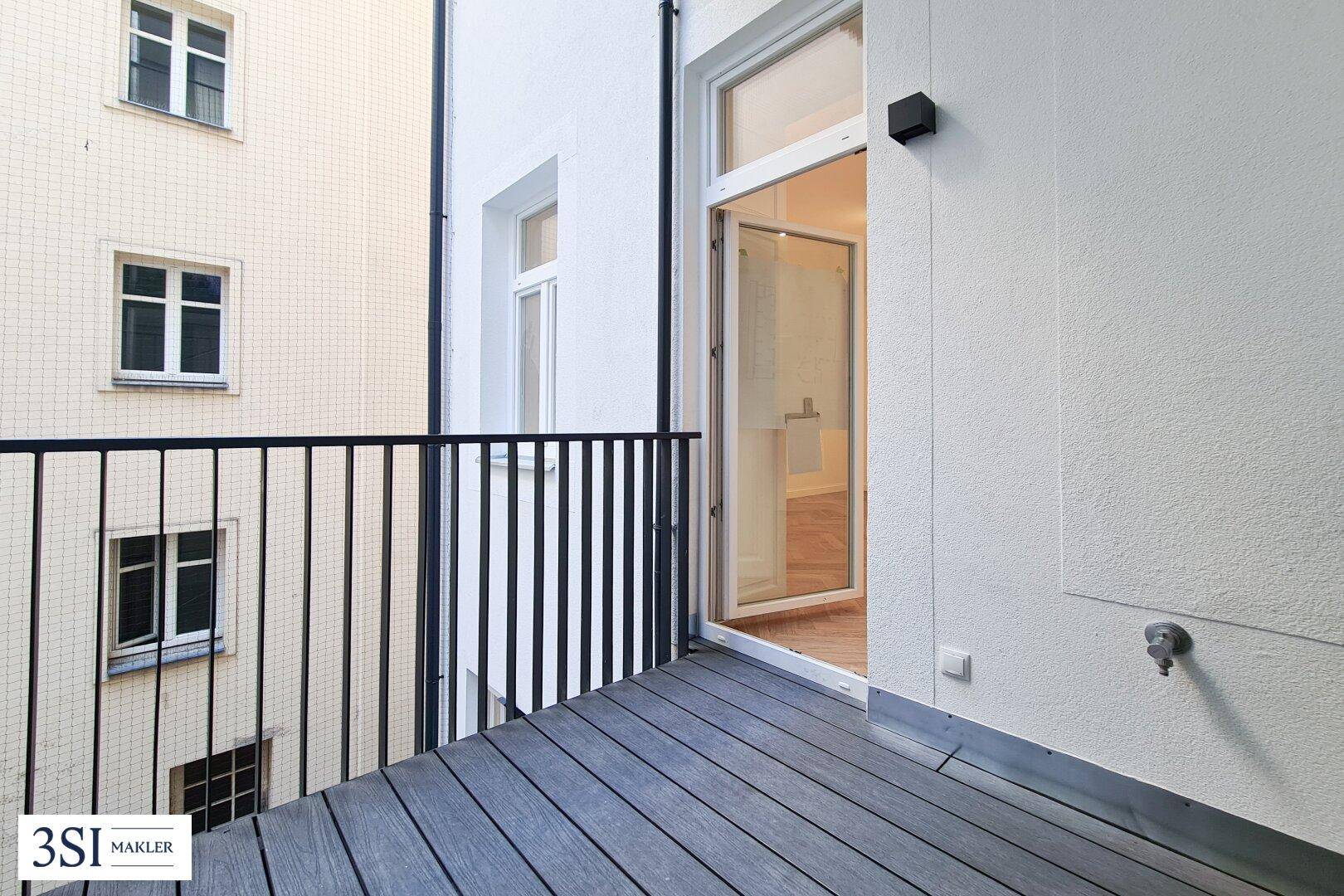 Kleiner Balkon mit dunklem Holzboden und schwarzem Geländer, mit Blick auf den Innenhof.