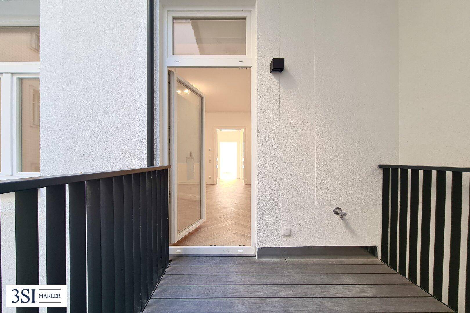 Balkon mit dunklem Holzboden und Blick in den hellen Innenraum der Wohnung.