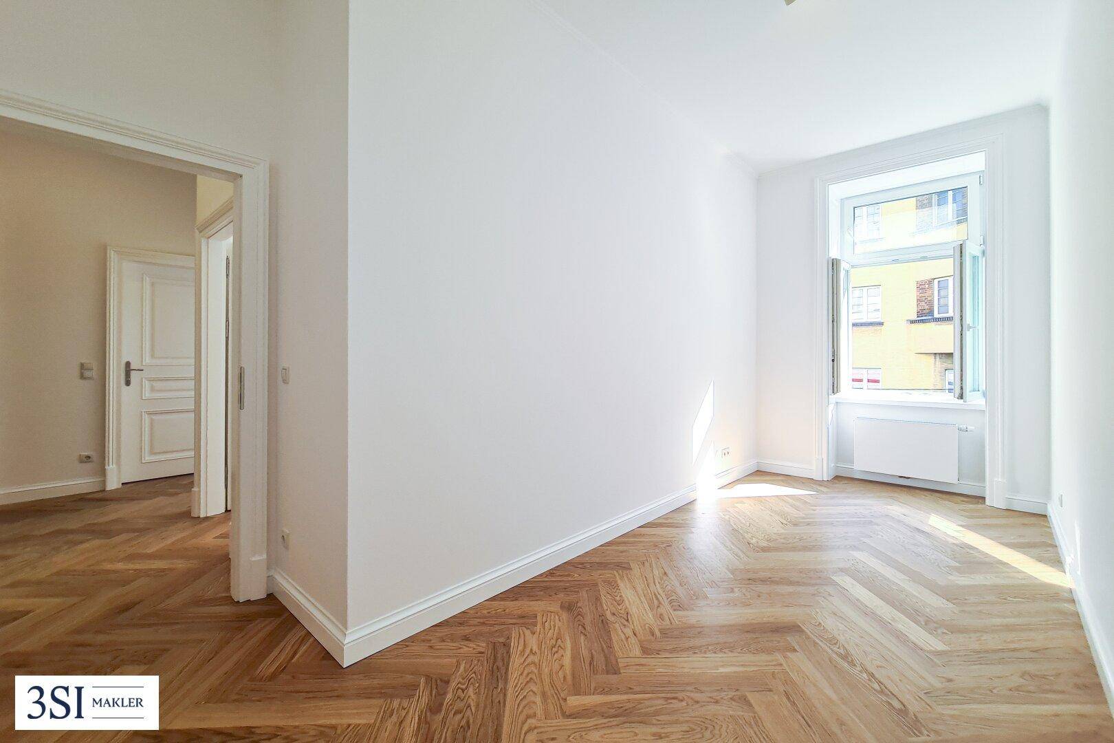 Helles Zimmer mit Fischgrätparkett und einem Fenster, das viel Tageslicht spendet.