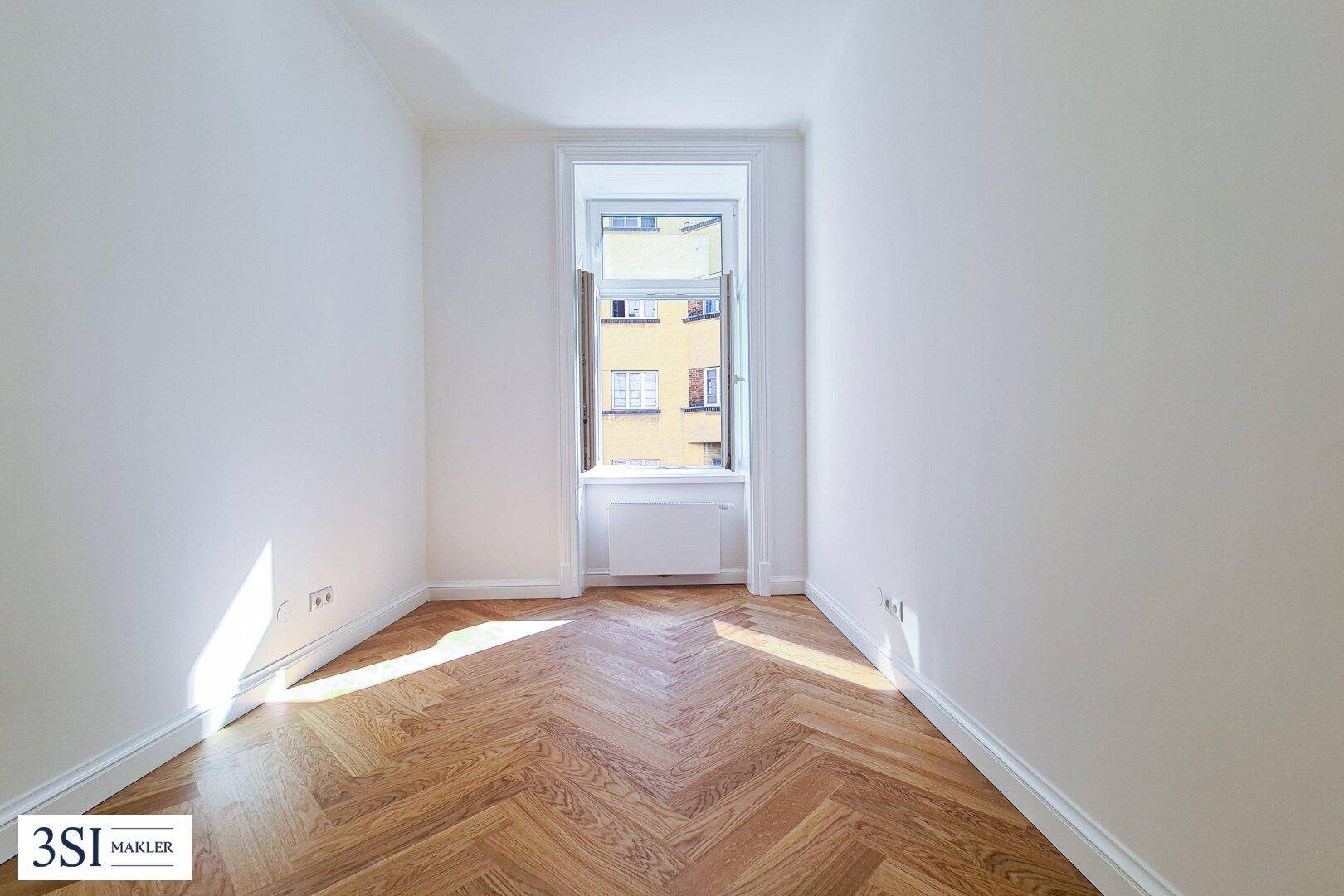 Kleiner, heller Raum mit Fischgrätparkett und einem Fenster zum Innenhof.