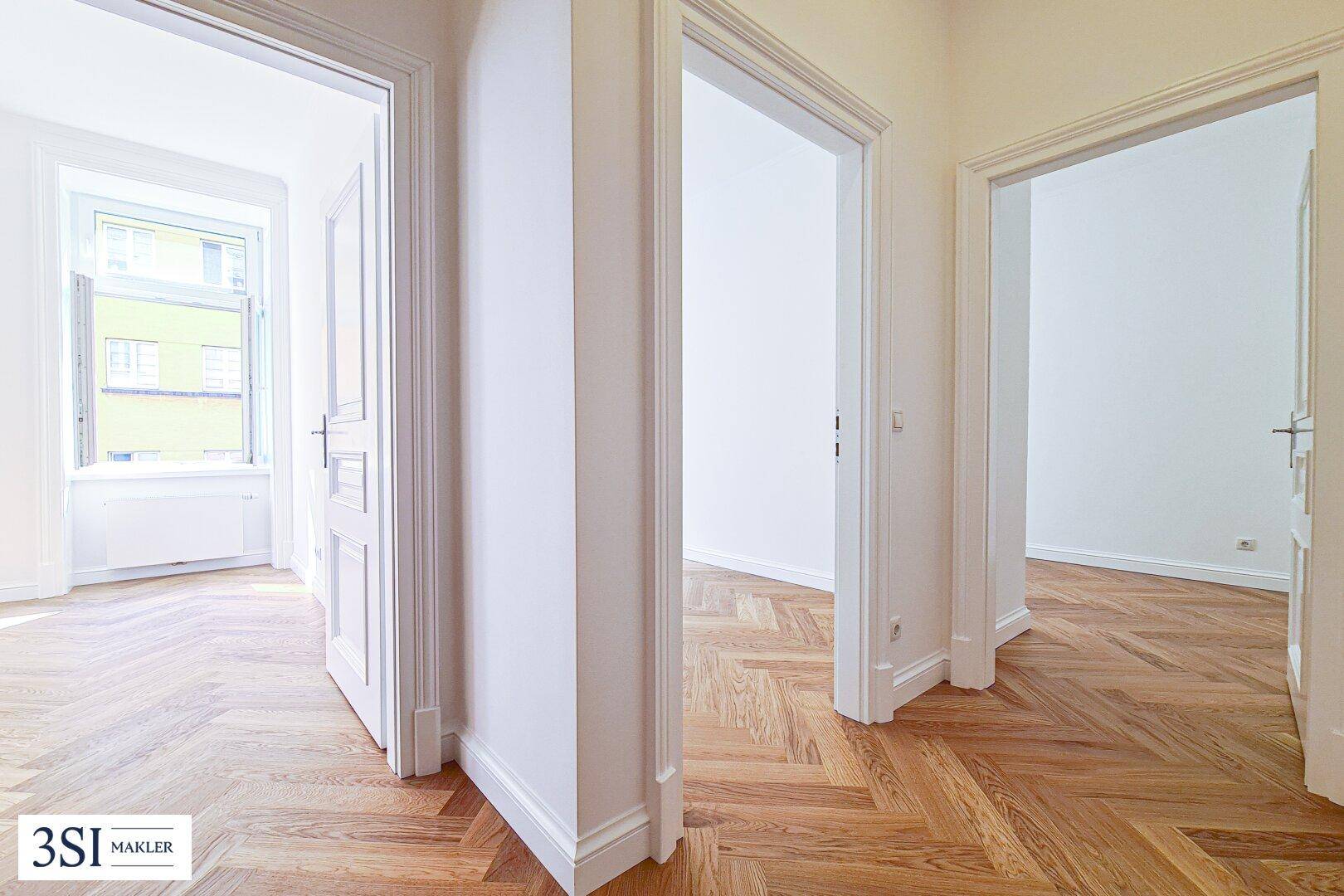 Heller Flur mit Fischgrätparkett und Zugang zu mehreren Zimmern der Wohnung.