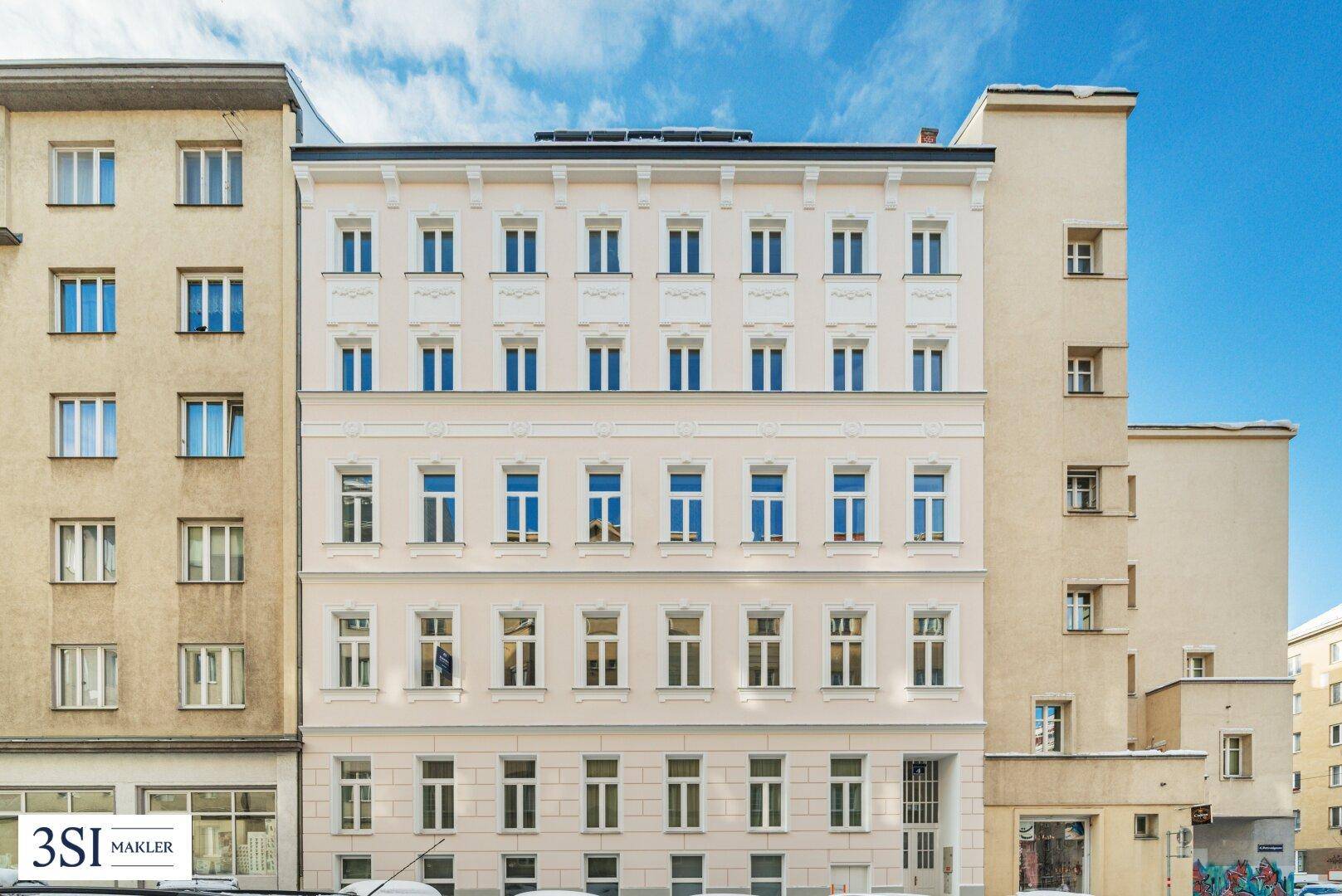 Renovierte Fassade eines Wohngebäudes mit vielen Fenstern unter blauem Himmel.