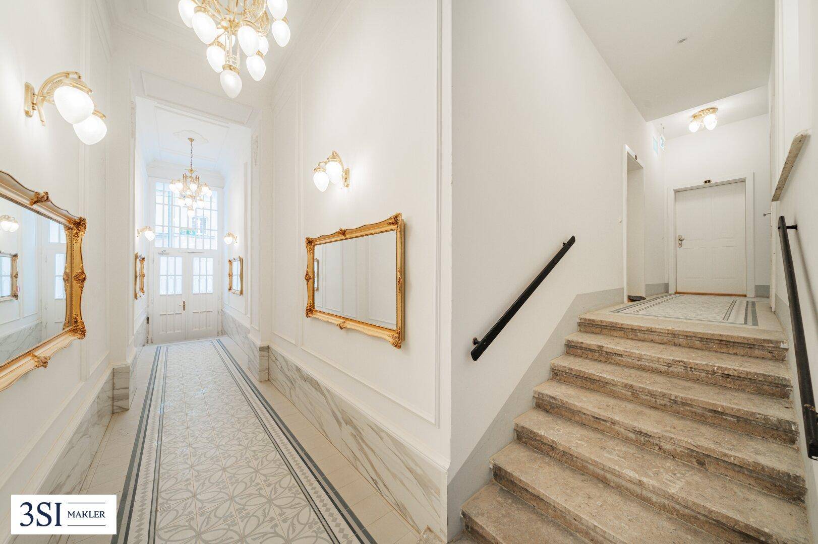 Elegantes Treppenhaus mit Marmorboden, goldenen Spiegeln und Kronleuchtern im Altbau.