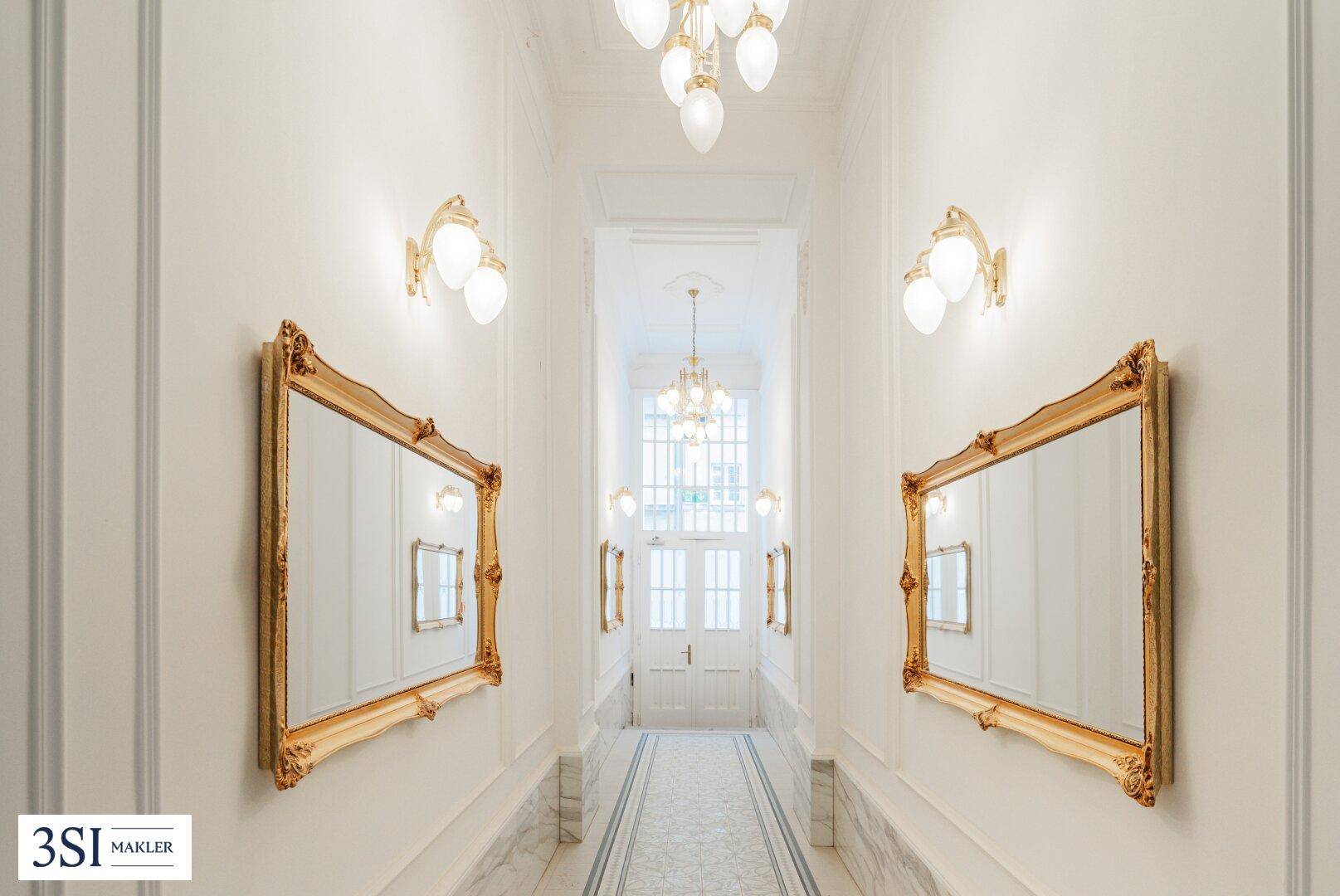 Repräsentativer Flur mit goldenen Spiegeln, Kronleuchter und Marmorboden im Altbau.