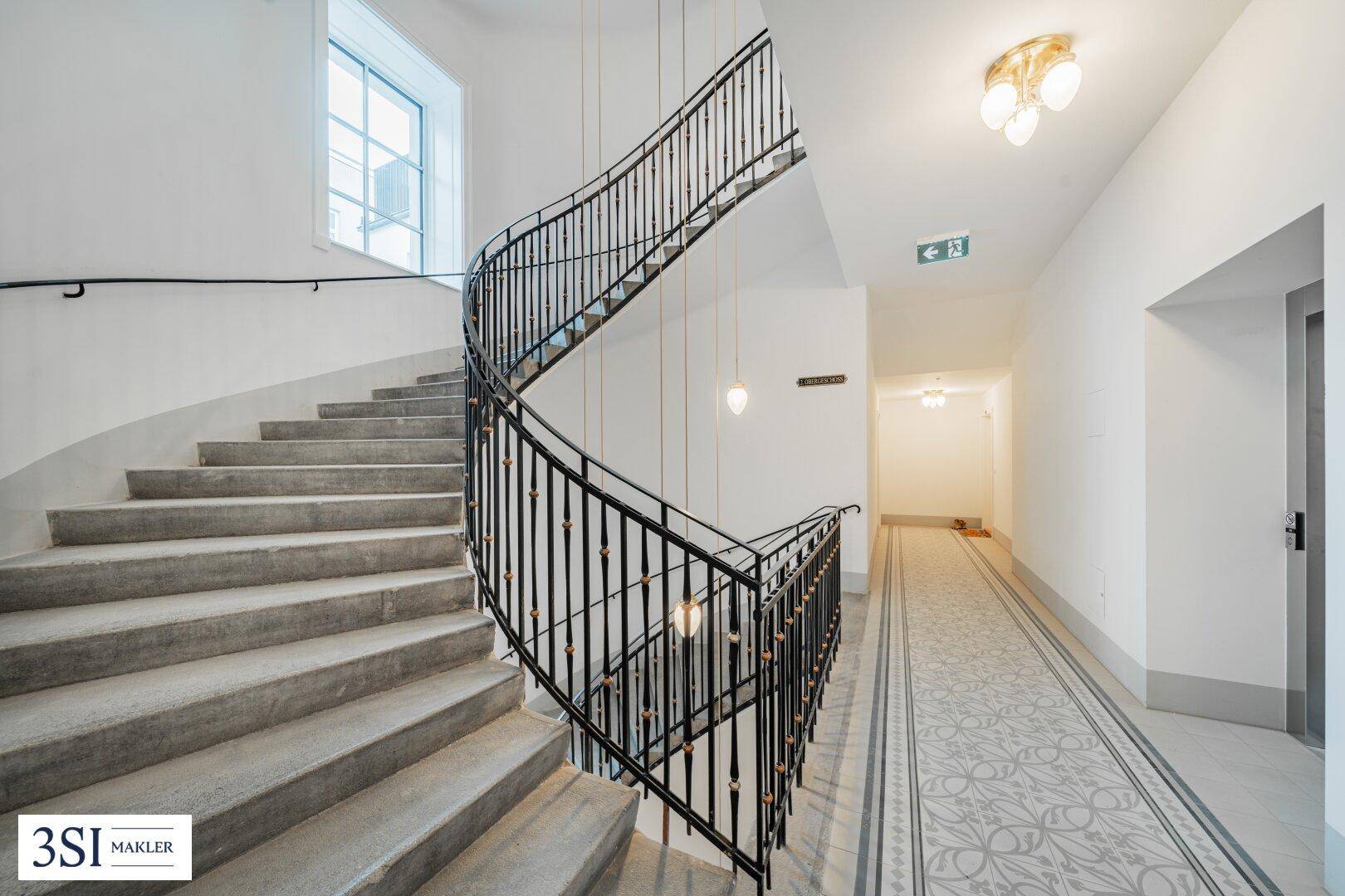 Elegantes Treppenhaus mit geschwungener Eisentreppe und Marmorboden in einem Altbau.