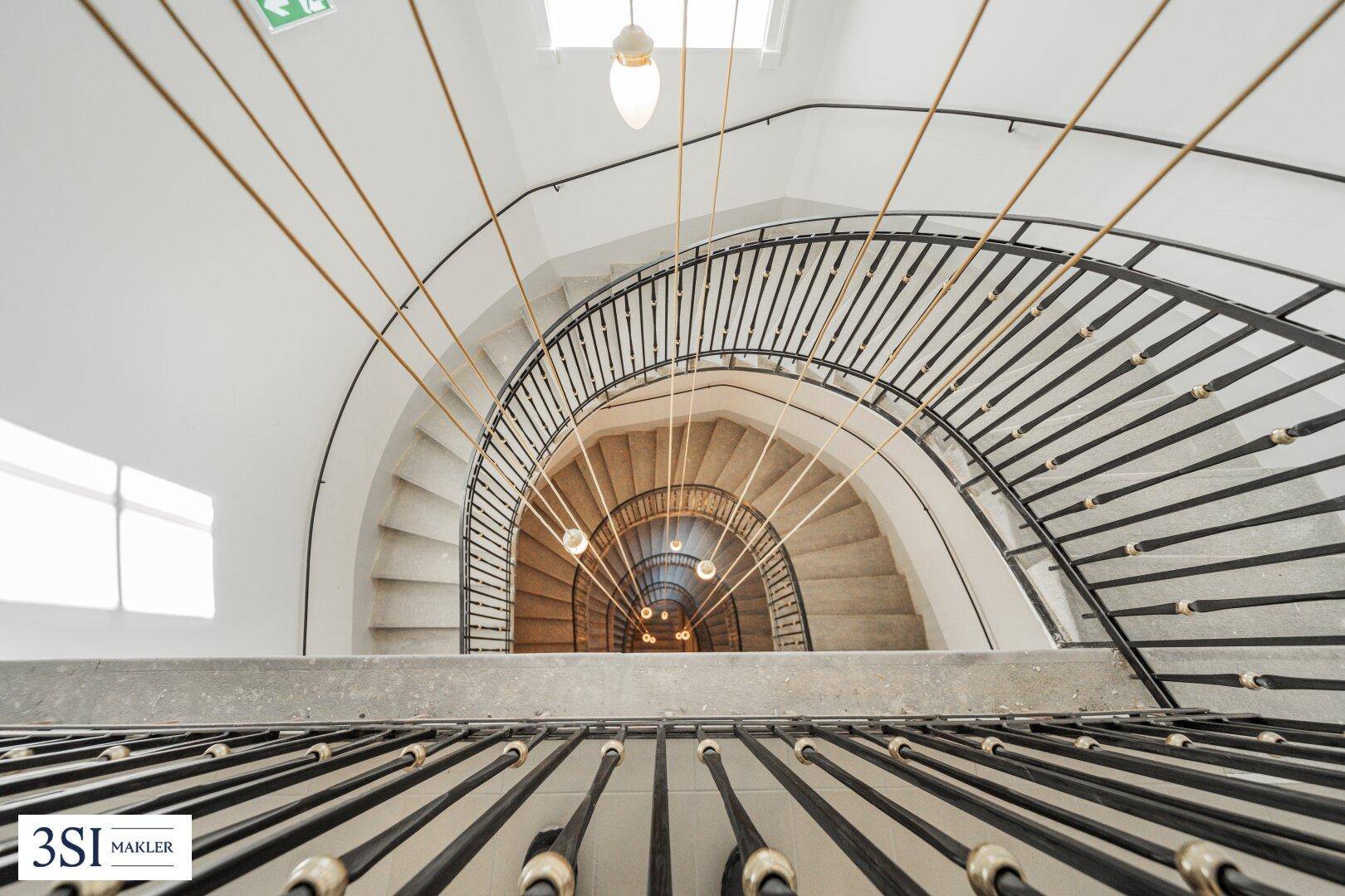 Blick von oben auf das elegante, geschwungene Treppenhaus mit schmiedeeisernem Geländer.