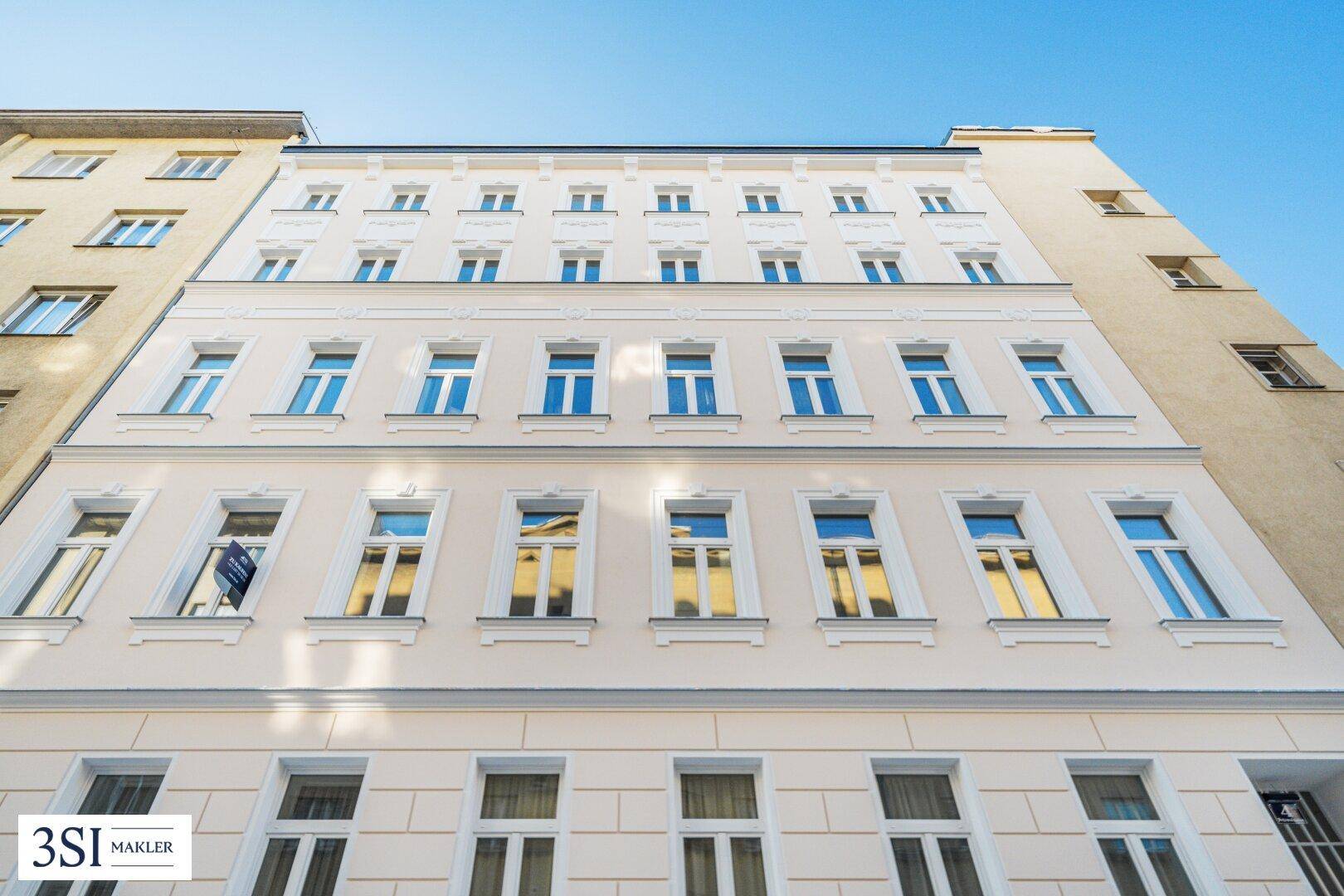 Renovierte Fassade eines Wohngebäudes mit vielen Fenstern unter blauem Himmel.