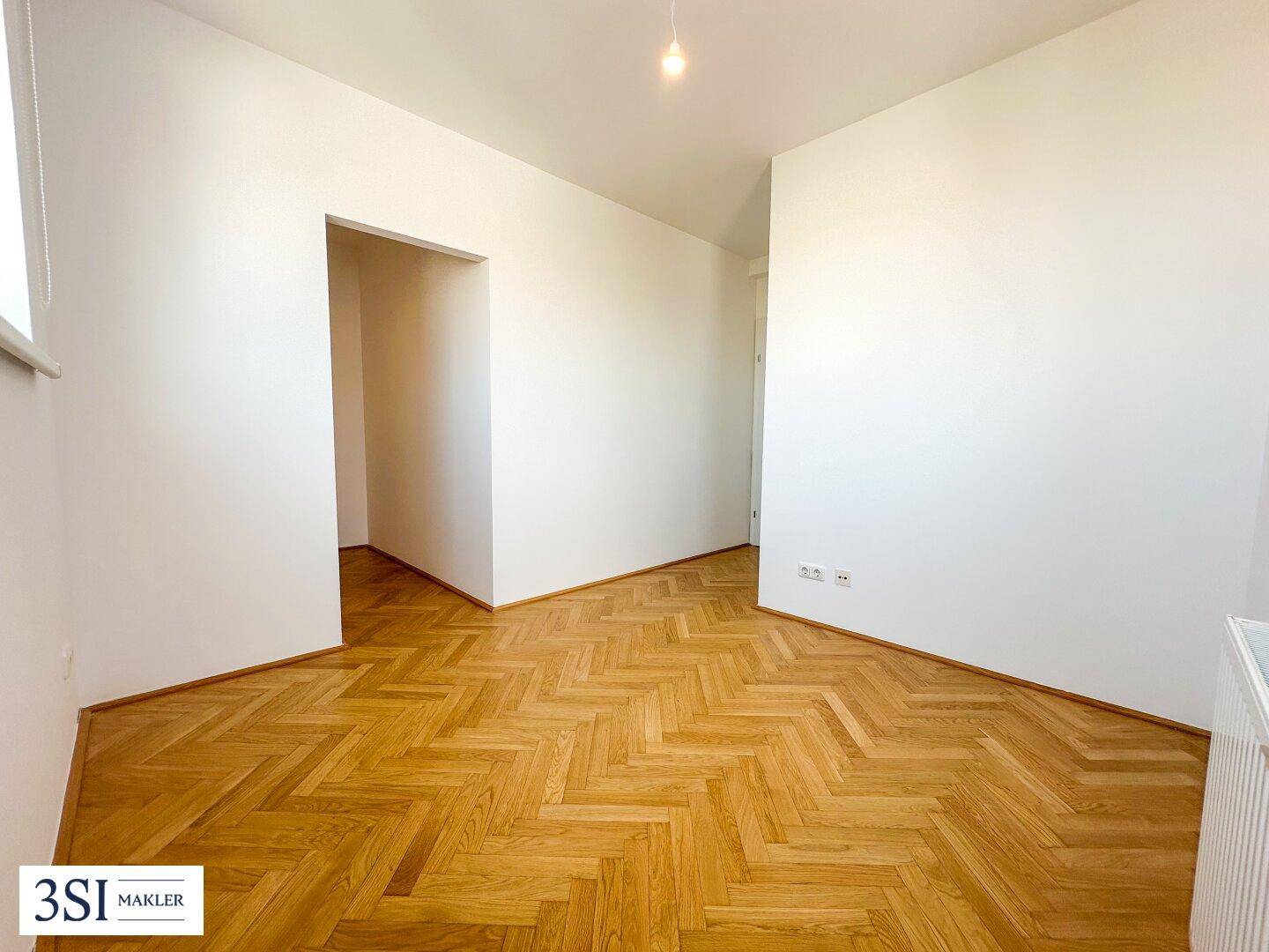 Leeres Zimmer mit Fischgrätparkett und weißen Wänden, bereit zur individuellen Gestaltung.