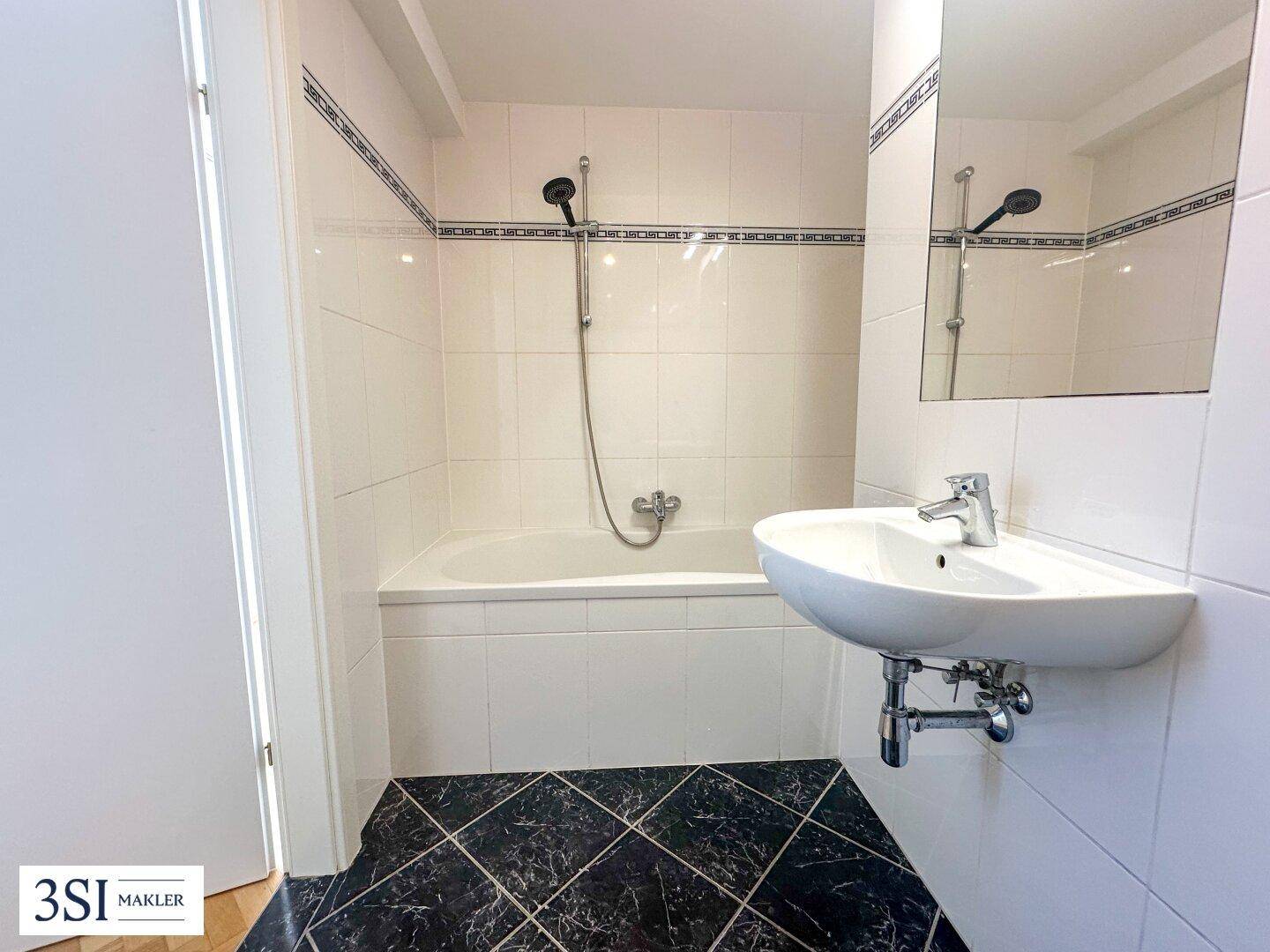 Badezimmer mit Badewanne, Waschbecken und weißen Fliesen, in gutem Zustand.