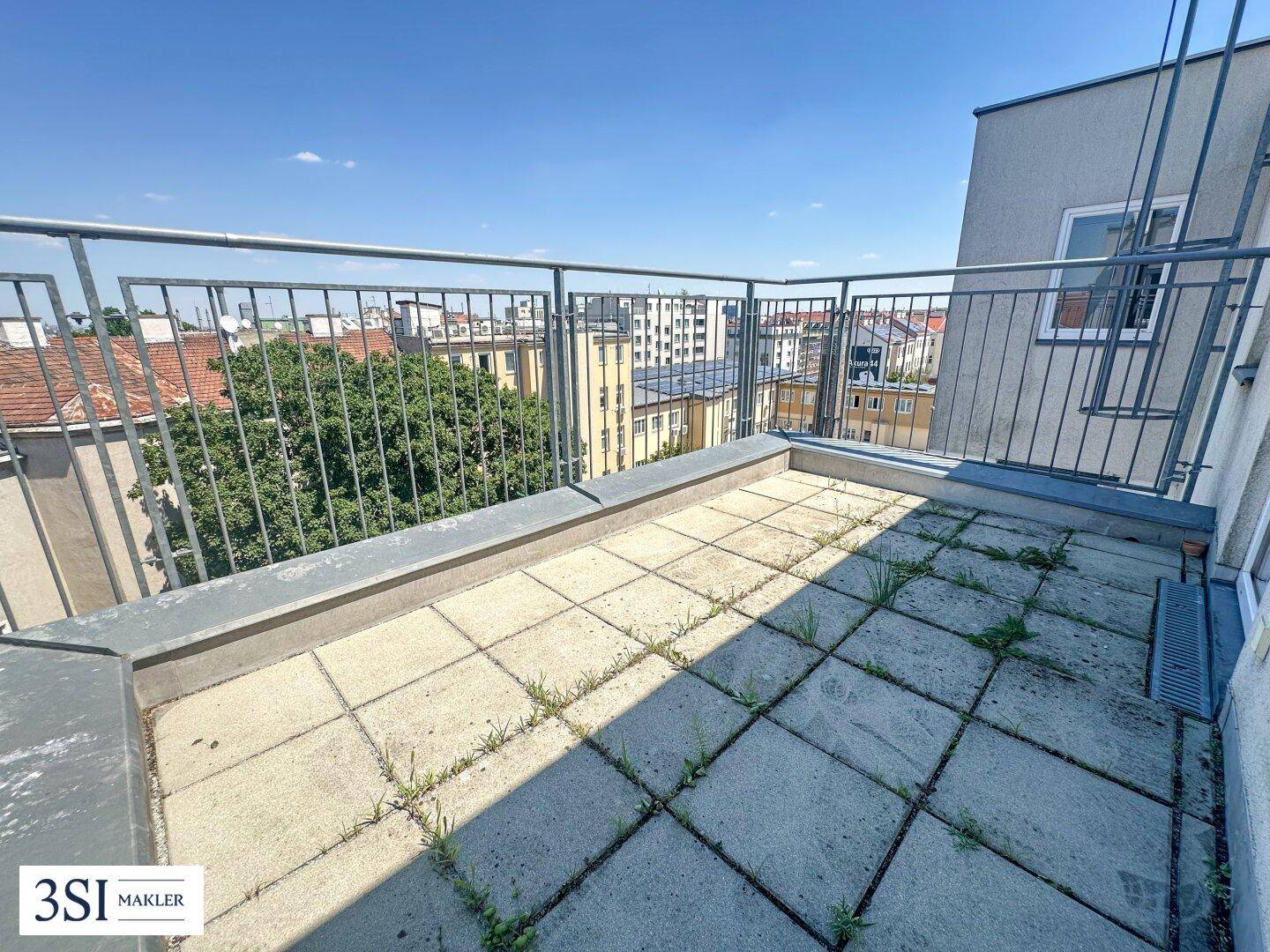 Sonniger Terrassenbereich mit Fliesenboden und weitem Blick über die Dächer der Stadt.