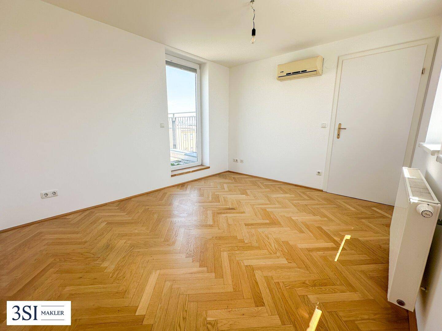 Helles Zimmer mit Parkettboden, Klimaanlage und Zugang zu einem kleinen Balkon.