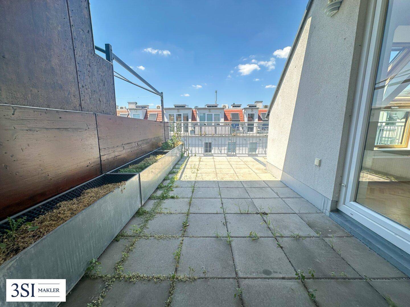 Sonniger Außenbereich mit Fliesenboden und integrierten Pflanzkästen.