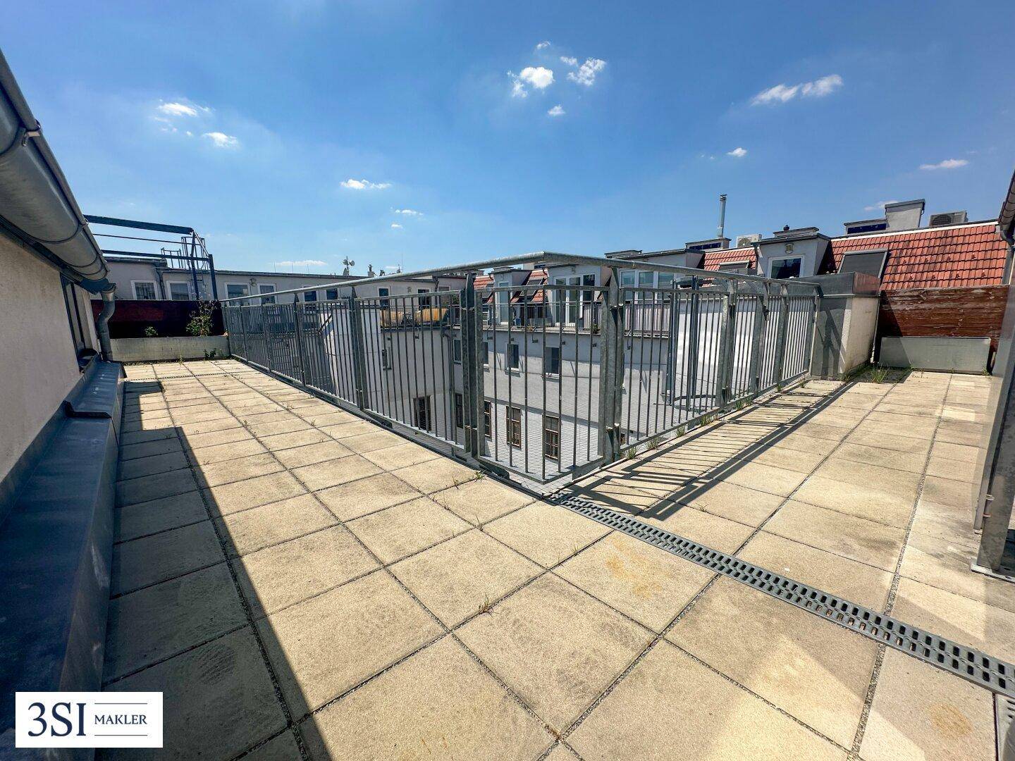 Unmöblierte Dachterrasse mit Fliesenboden und Blick auf umliegende Gebäude.
