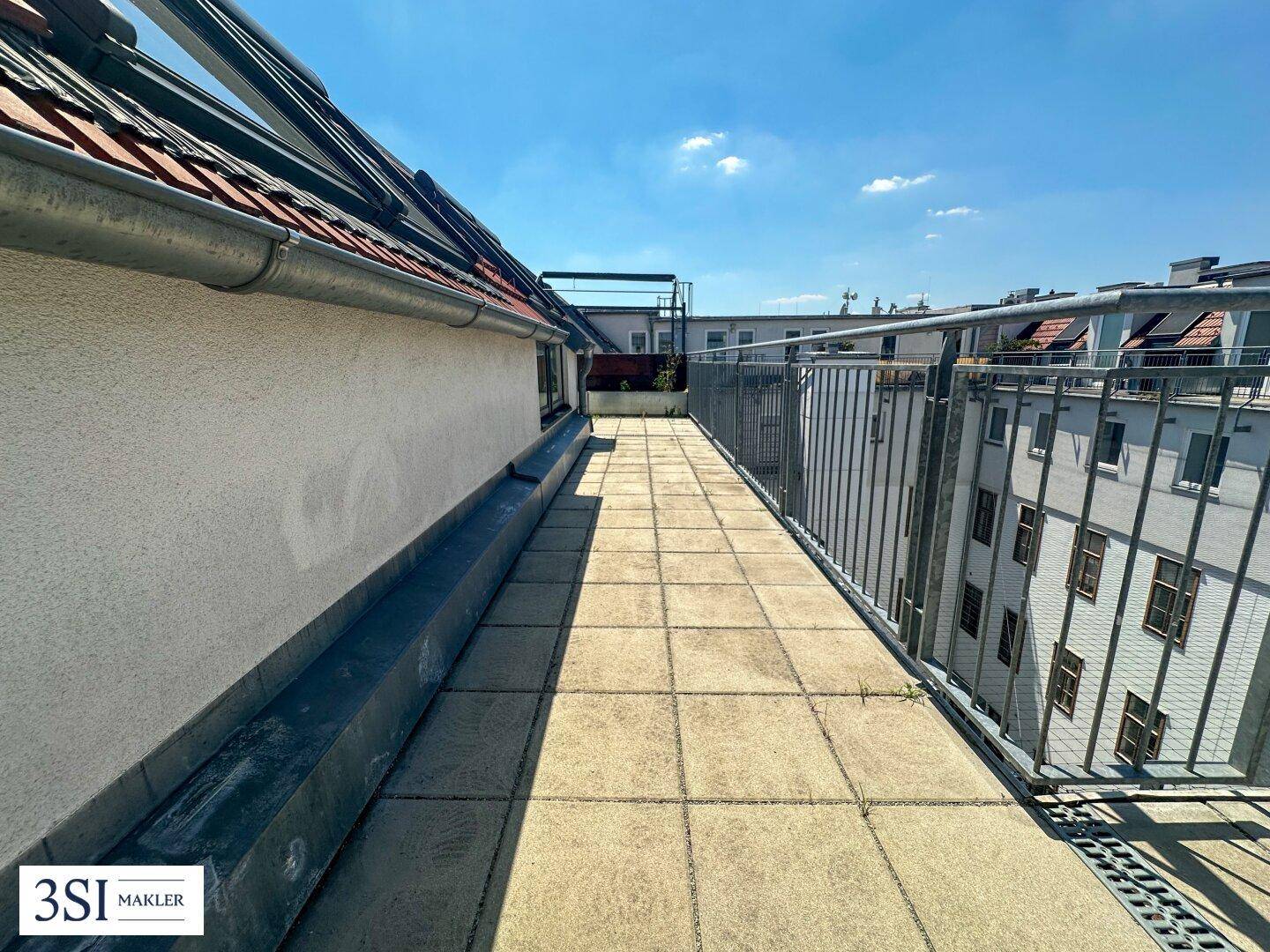 Langer, schmaler Terrassenbereich mit Fliesenboden und Blick auf die Nachbargebäude.