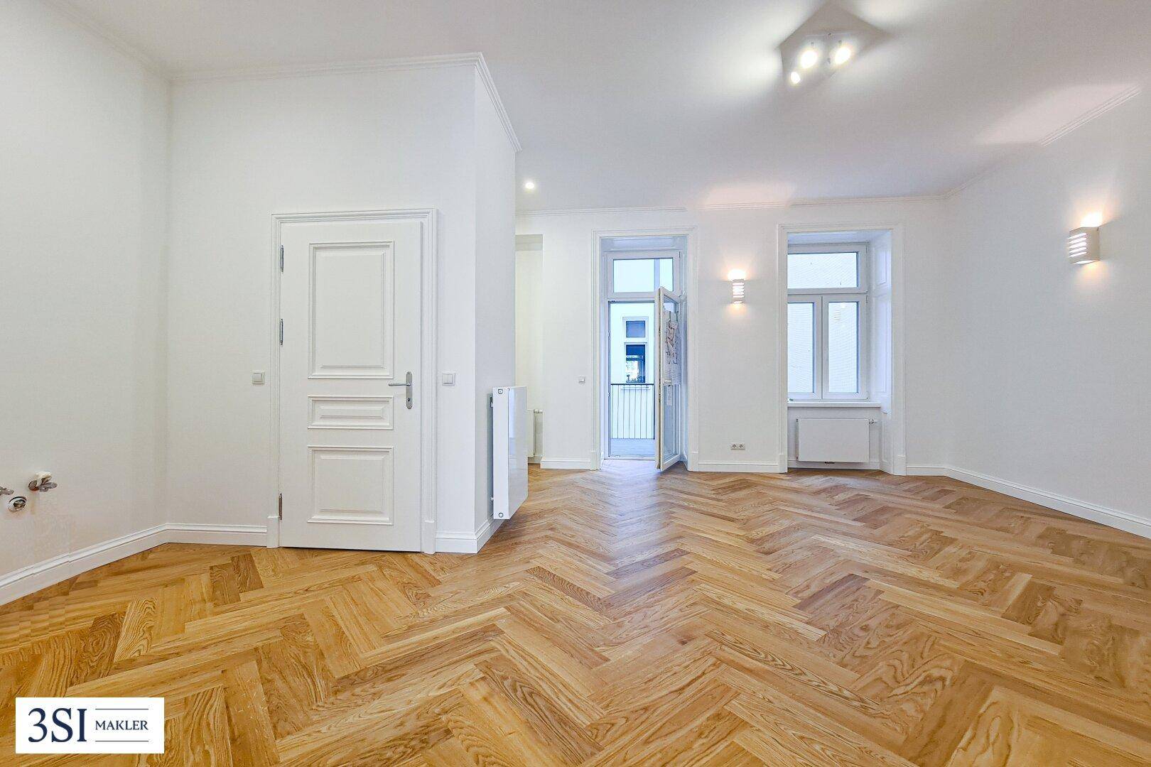 Geräumiges Zimmer mit Fischgrätparkett, weißen Wänden und Zugang zu einem Balkon.