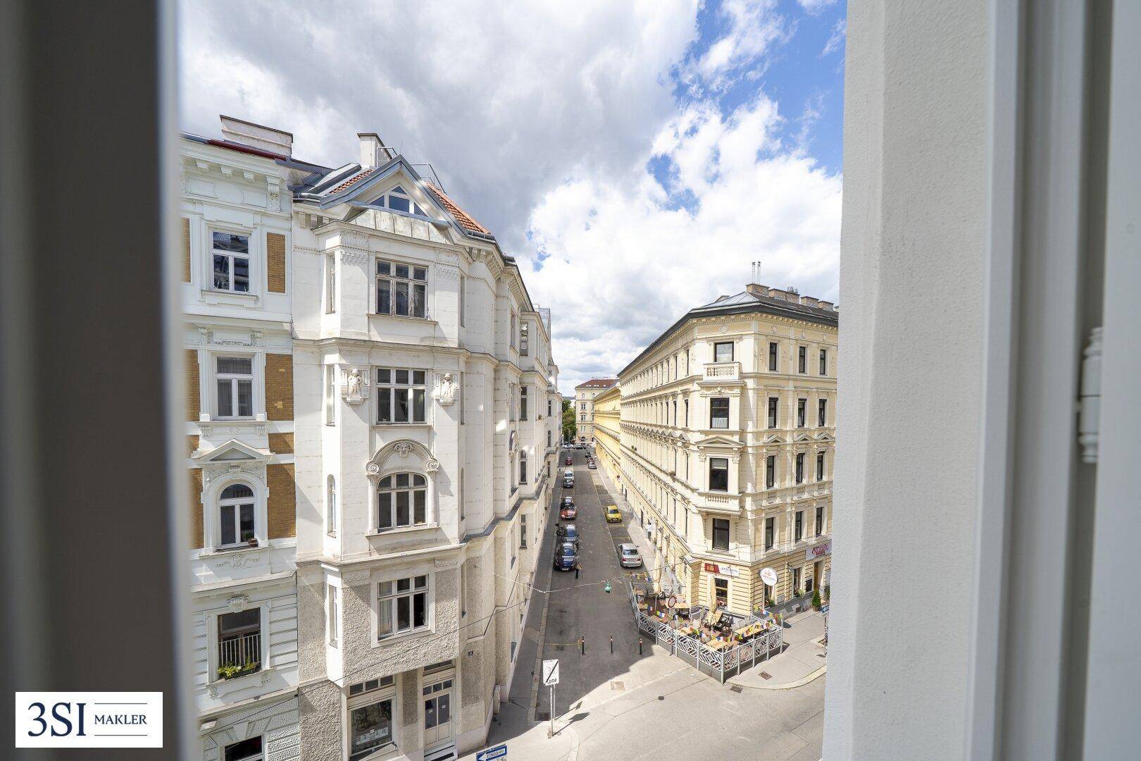 Blick aus dem Fenster auf eine belebte Straße mit historischen Gebäuden und Geschäften.