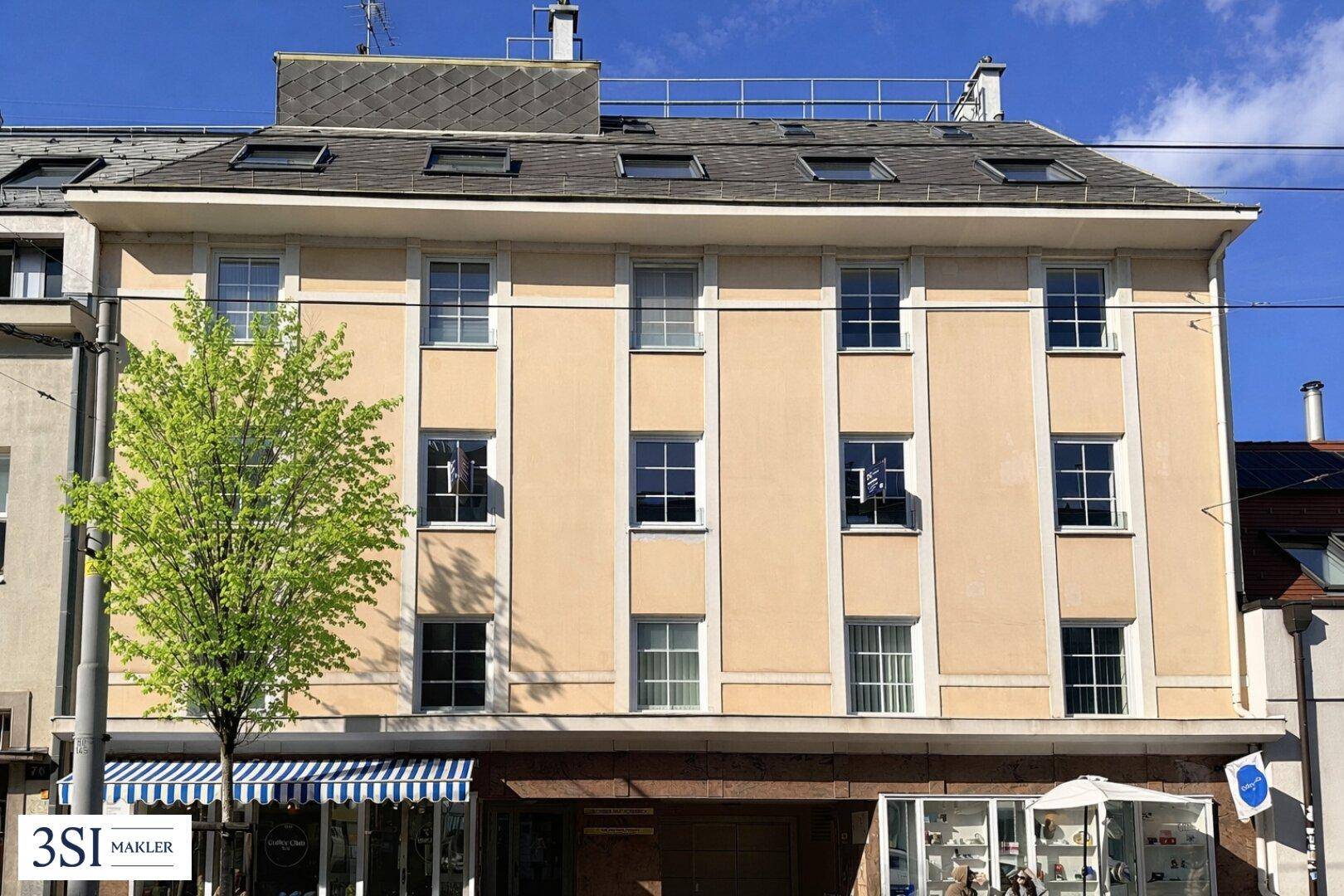 Fassade eines Mehrfamilienhauses mit vielen Fenstern und Geschäften im Erdgeschoss.