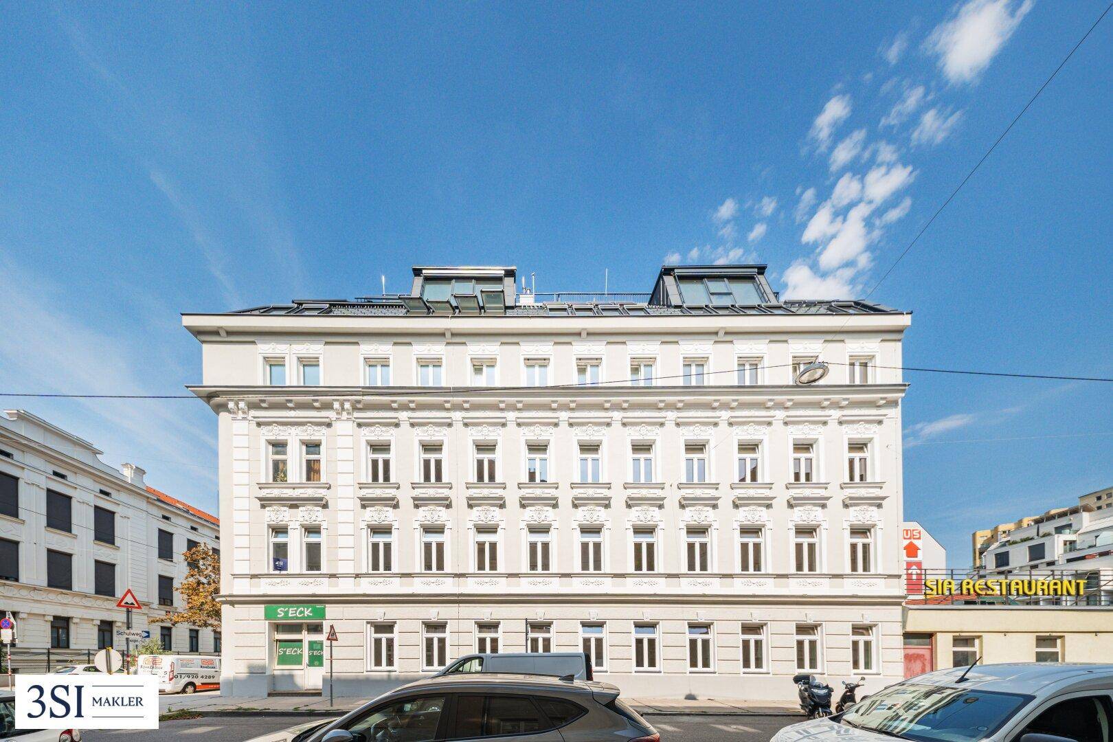 Klassische Fassade eines Mehrfamilienhauses mit vielen Fenstern und modernen Dachaufbauten in der Stadt.