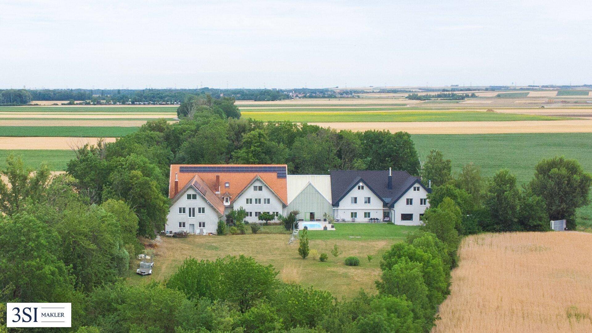 Luftaufnahme eines weitläufigen Anwesens mit mehreren Gebäuden, umgeben von Feldern und viel Grün.