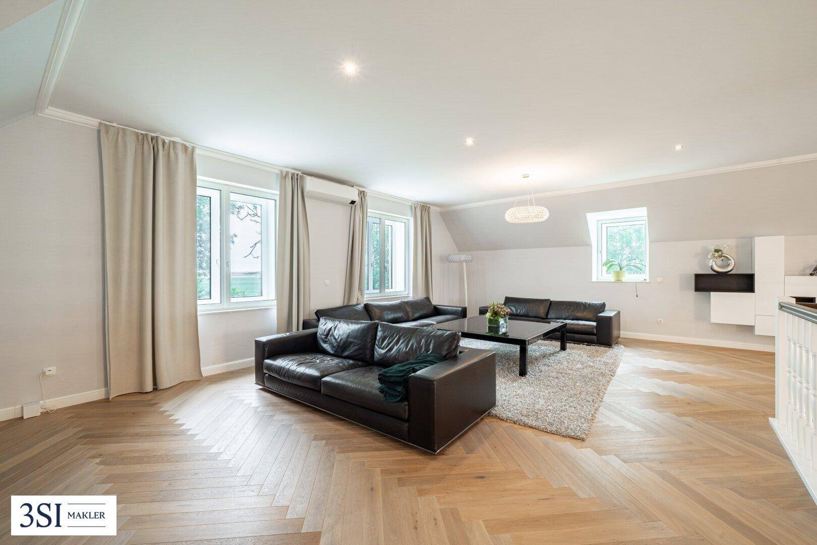 Großes Wohnzimmer im Dachgeschoss mit Fischgrätparkett, bequemen Sofas und vielen Fenstern.