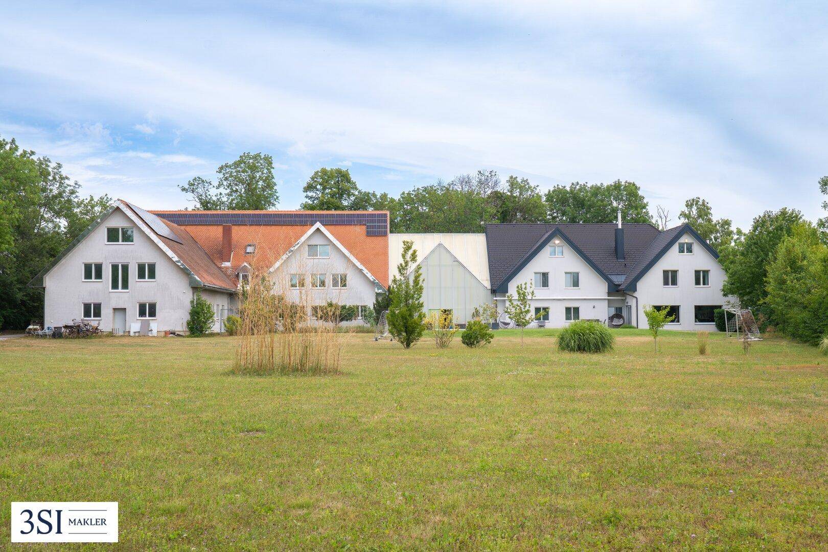 Weitläufiger Gartenbereich mit Rasenfläche und Blick auf das Anwesen mit mehreren Gebäuden.