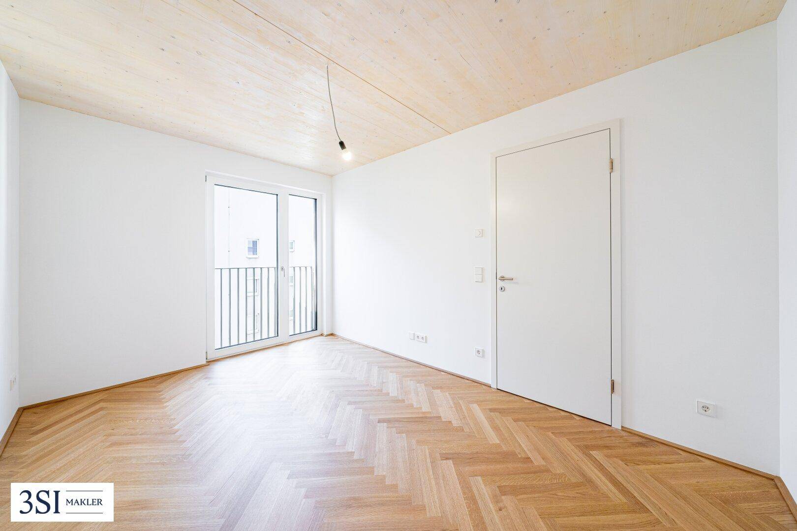 Unmöblierter Raum mit Holzboden und Balkontür, bereit zur individuellen Gestaltung und Nutzung.