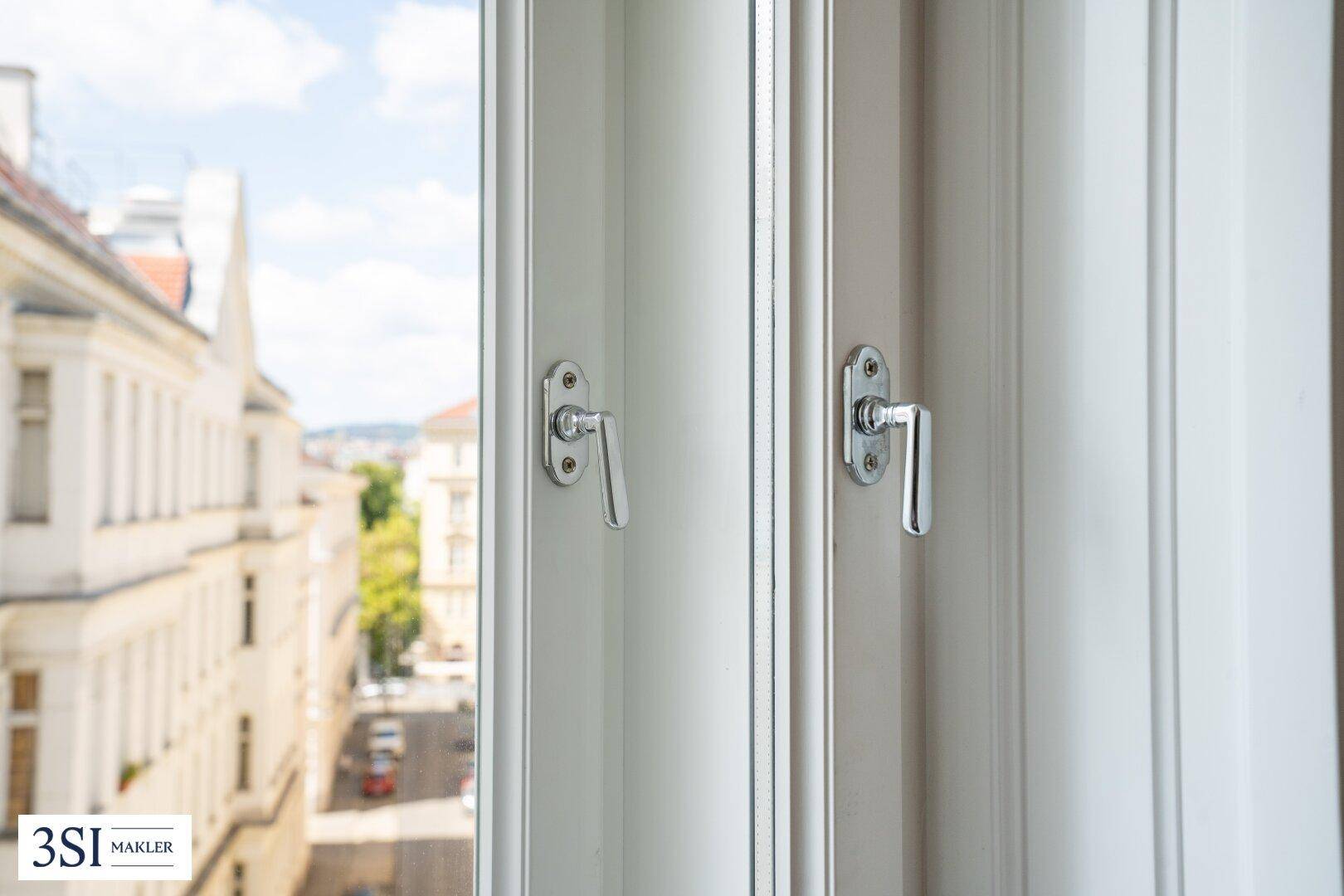 Blick aus einem Fenster auf eine belebte Straße mit historischen Gebäuden und Bäumen.