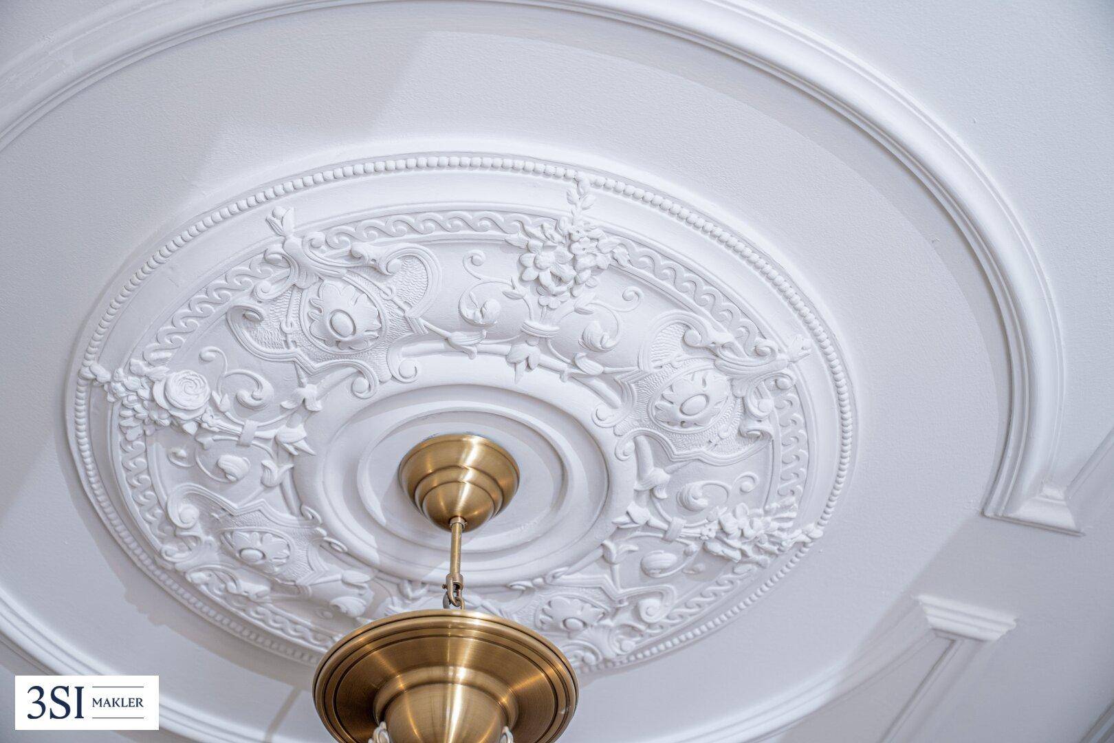 Detailaufnahme einer kunstvoll verzierten Stuckdecke mit einem eleganten Messing-Kronleuchter.