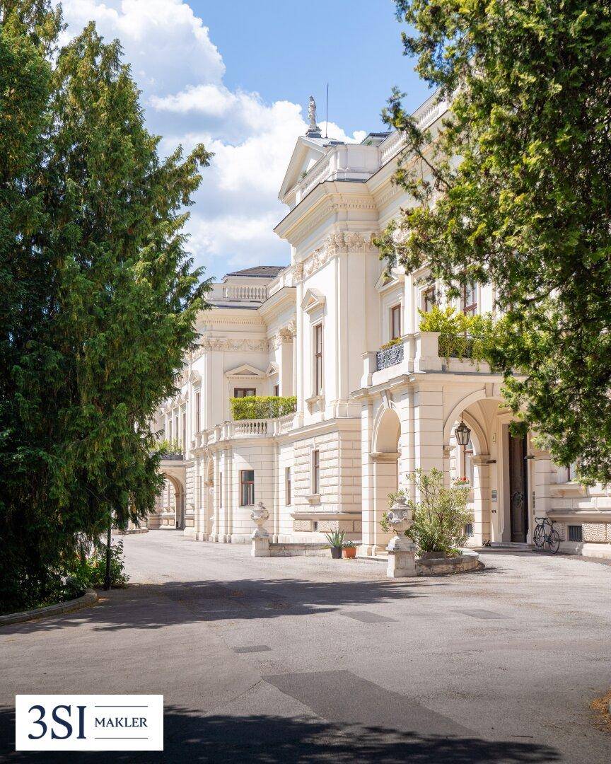 Prächtiges historisches Gebäude mit klassischer Architektur, umgeben von altem Baumbestand und einer Zufahrt.