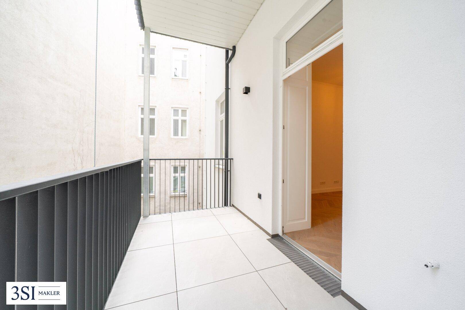 Heller Balkon mit Fliesenboden und Blick auf den ruhigen Innenhof, ideal für entspannte Stunden im Freien.