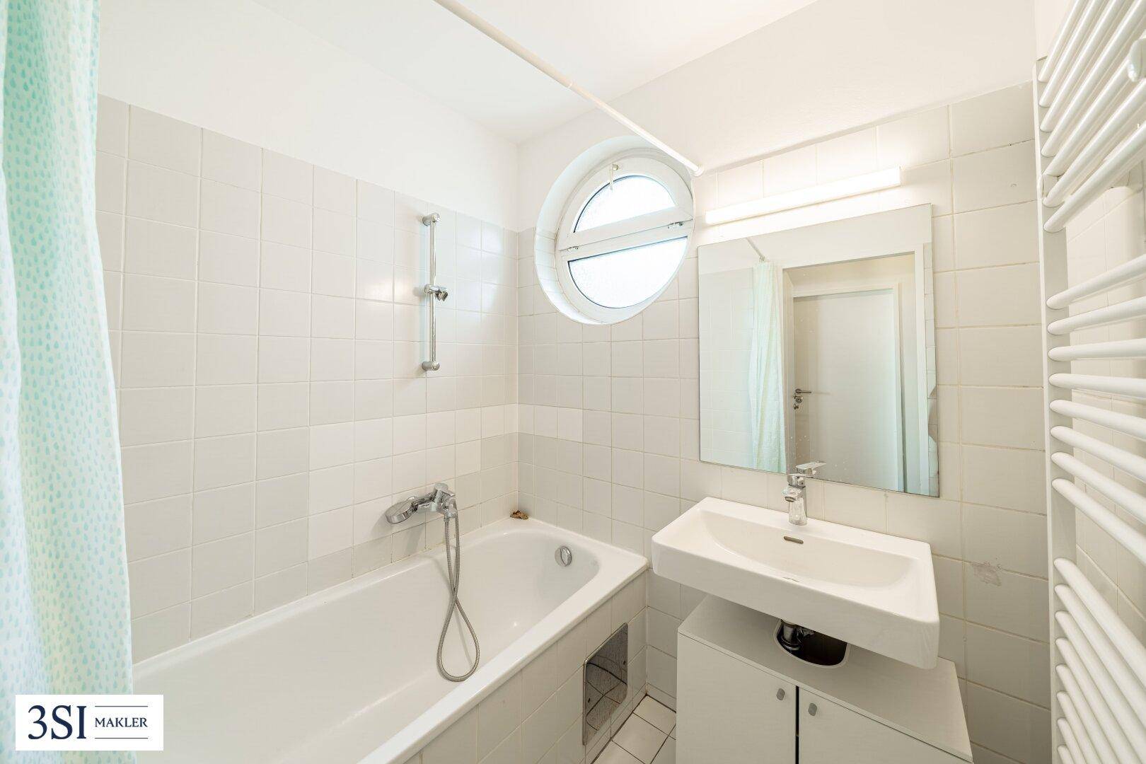 Helles Badezimmer mit Badewanne, Waschbecken und einem runden Fenster für Tageslicht.