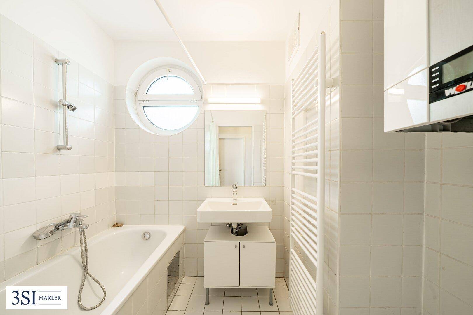 Funktionales Badezimmer mit Badewanne, Handtuchheizkörper und einem runden Fenster.