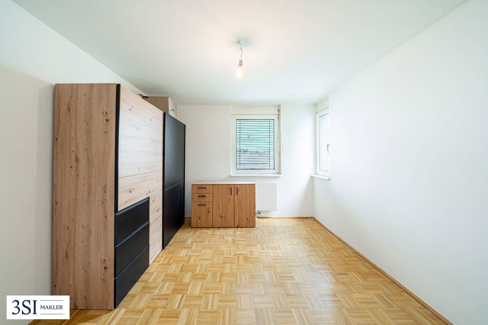Schlafzimmer mit Parkettboden, Fenster und modernen Holzschränken für ausreichend Stauraum.
