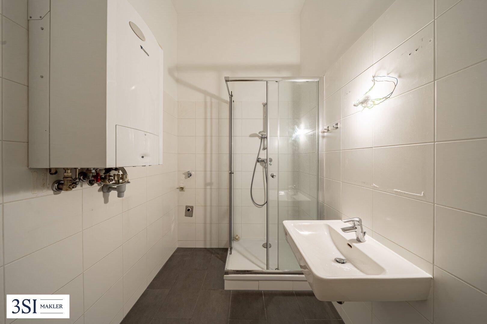 Helles Badezimmer mit Duschkabine, Waschbecken und einem Warmwasserbereiter an der Wand.