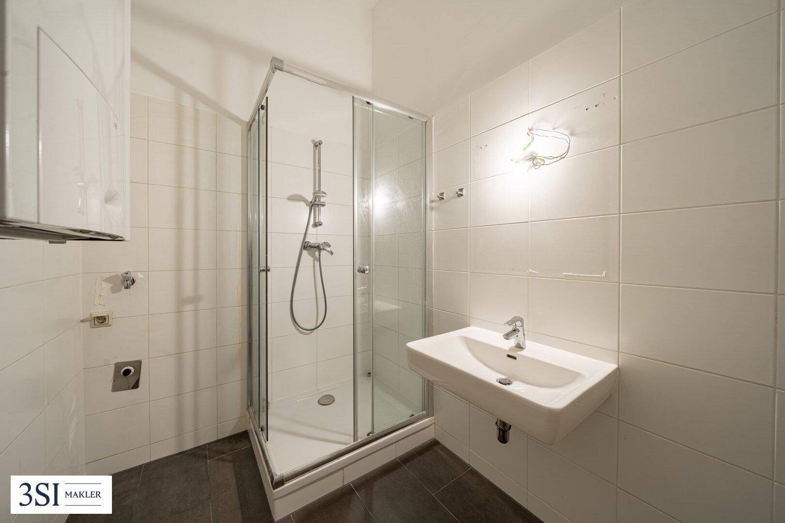 Funktionales Badezimmer mit Duschkabine, Waschbecken und weißen Fliesen an den Wänden.