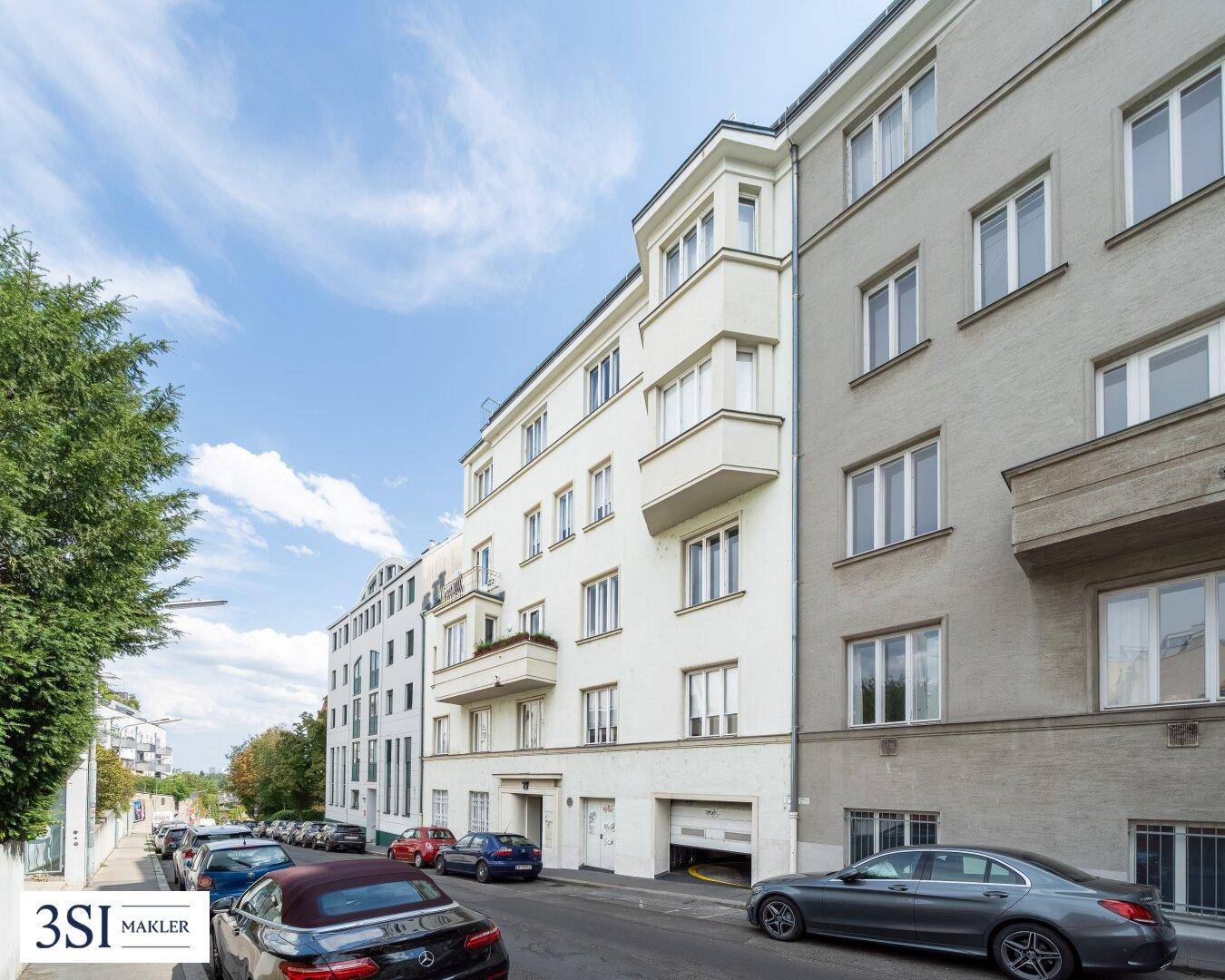 Mehrstöckiges Wohngebäude mit klassischer Fassade, Balkonen und parkenden Autos auf der Straße.