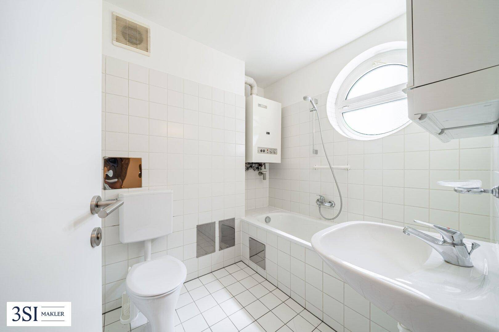 Helles Badezimmer mit weißen Fliesen, Badewanne, WC und einem markanten runden Fenster.