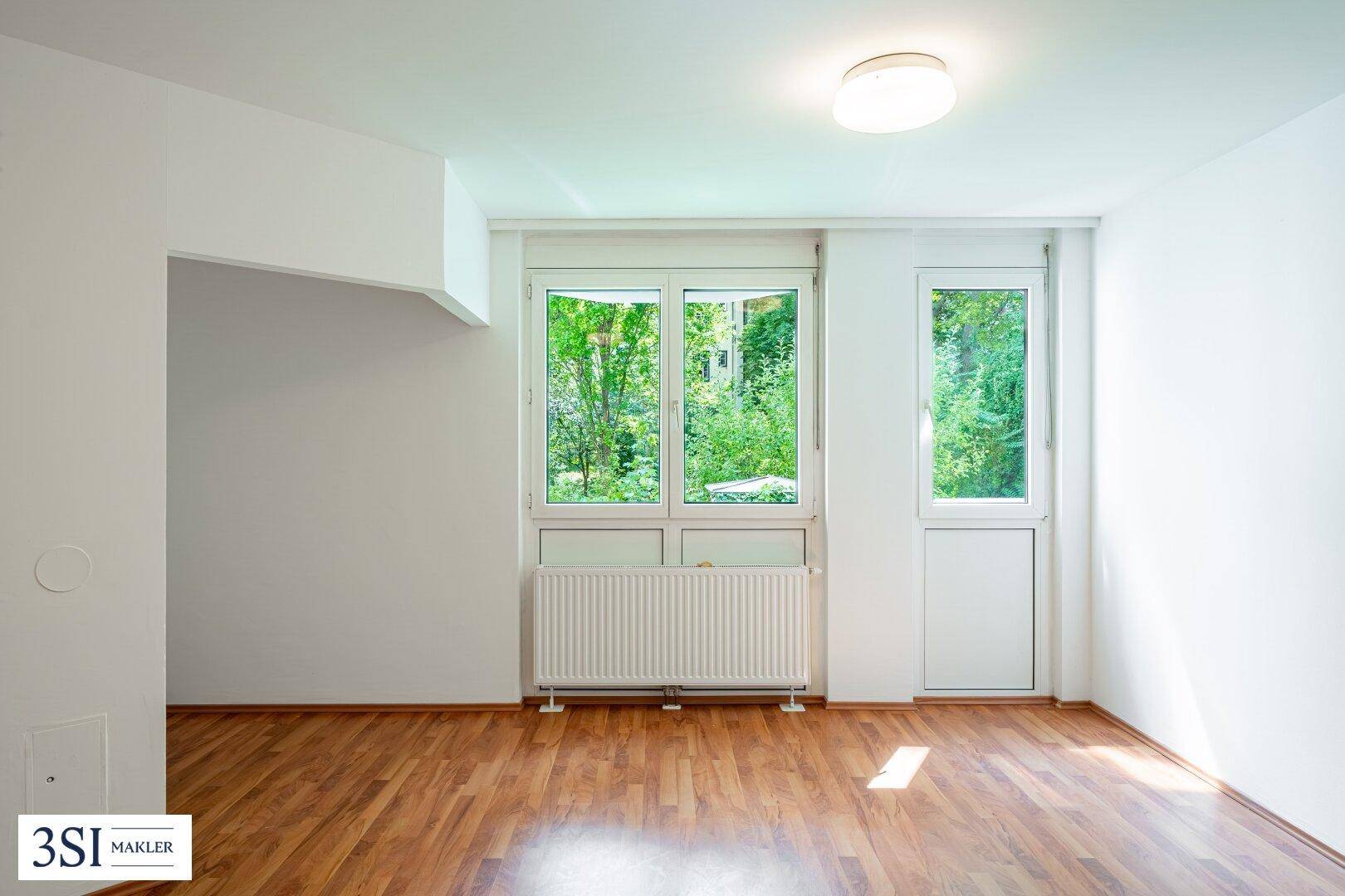 Große Fensterfront in einem hellen Raum, die viel Tageslicht und einen Blick ins Grüne bietet.