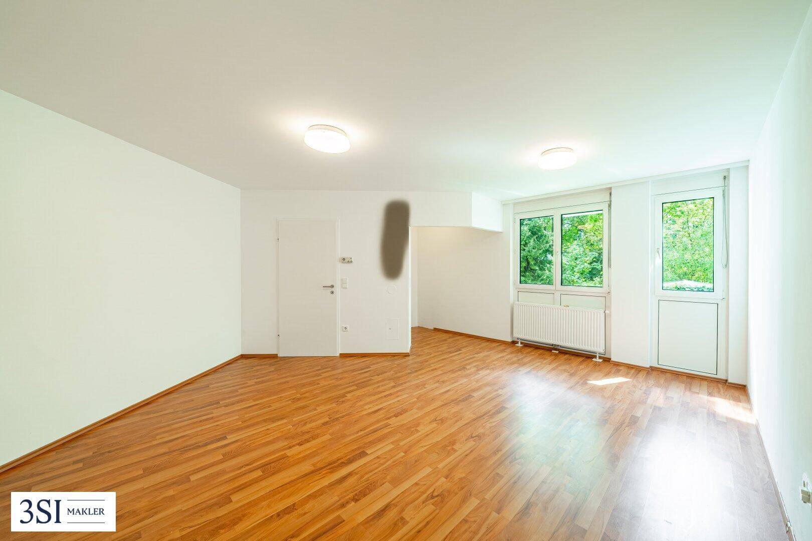 Geräumiges, unmöbliertes Zimmer mit warmem Holzboden und großen Fenstern zum Garten.