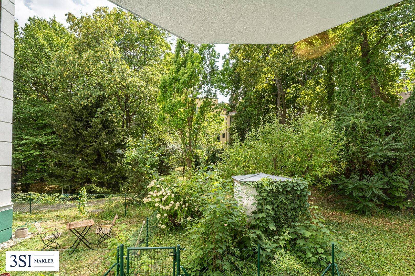 Üppiger grüner Gartenbereich mit kleiner Sitzecke, von einem Balkon oder einer Terrasse aus gesehen.