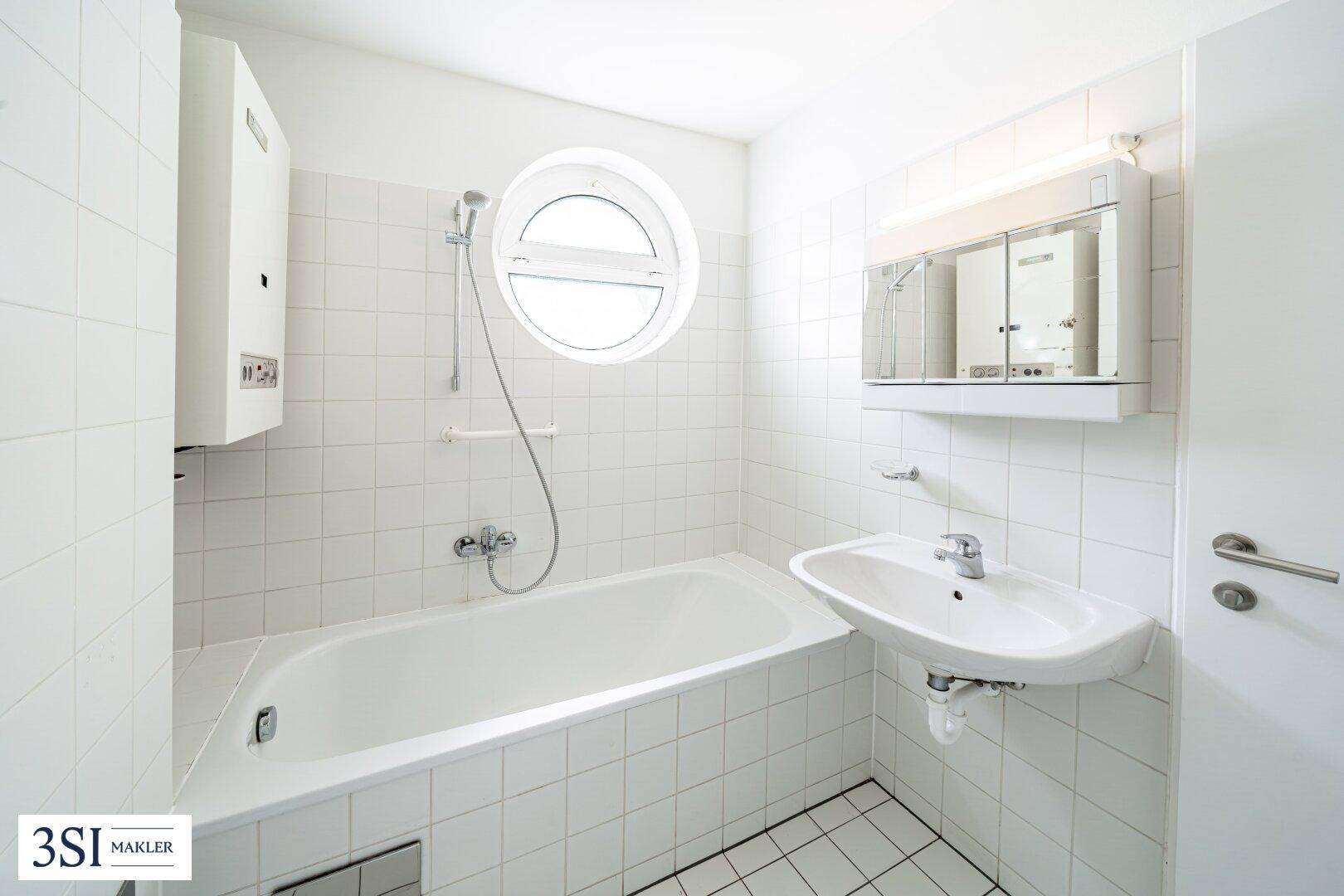 Funktionales Badezimmer mit Badewanne, Waschbecken und einem runden Fenster, alles in Weiß gehalten.