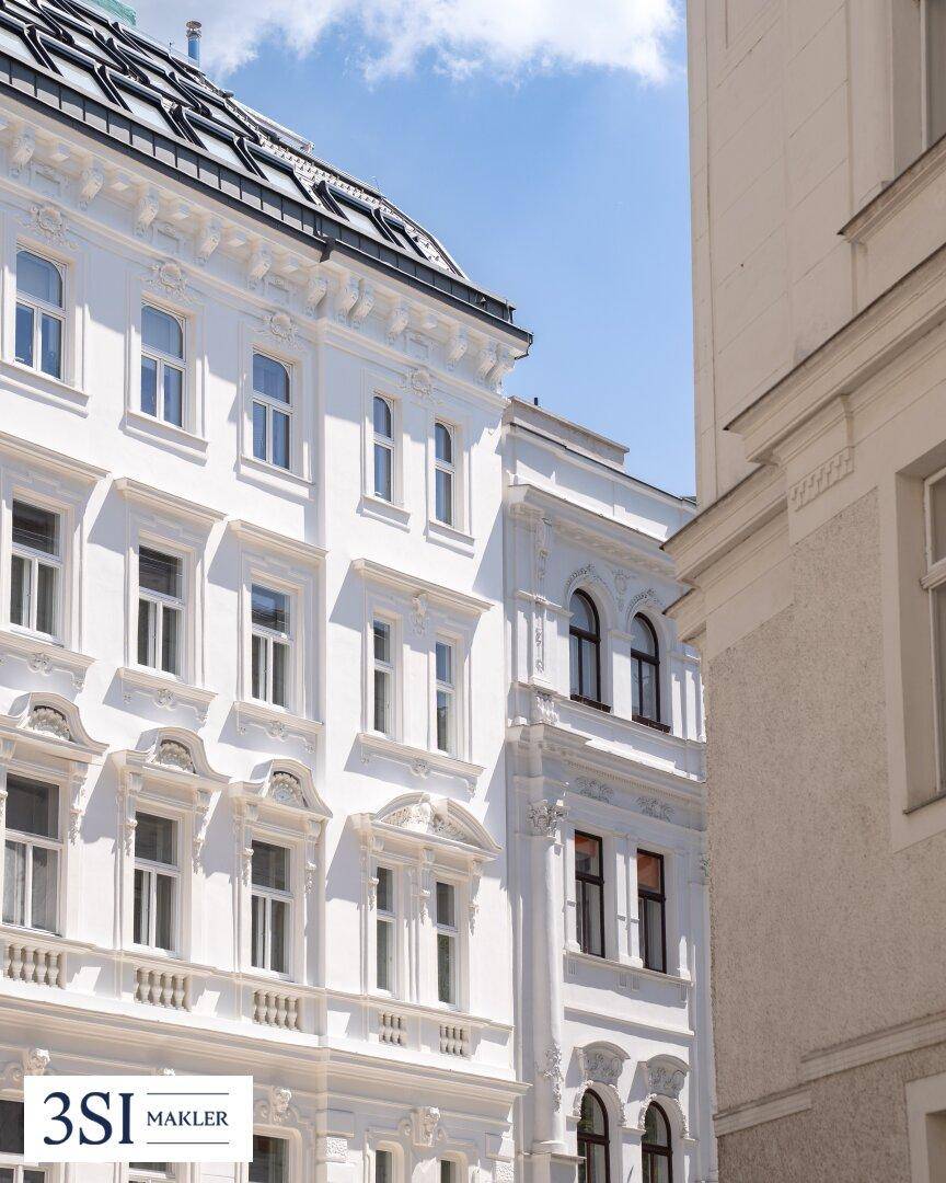 Detailansicht einer eleganten, weißen Fassade mit reich verzierten Fenstern und Stuckelementen.
