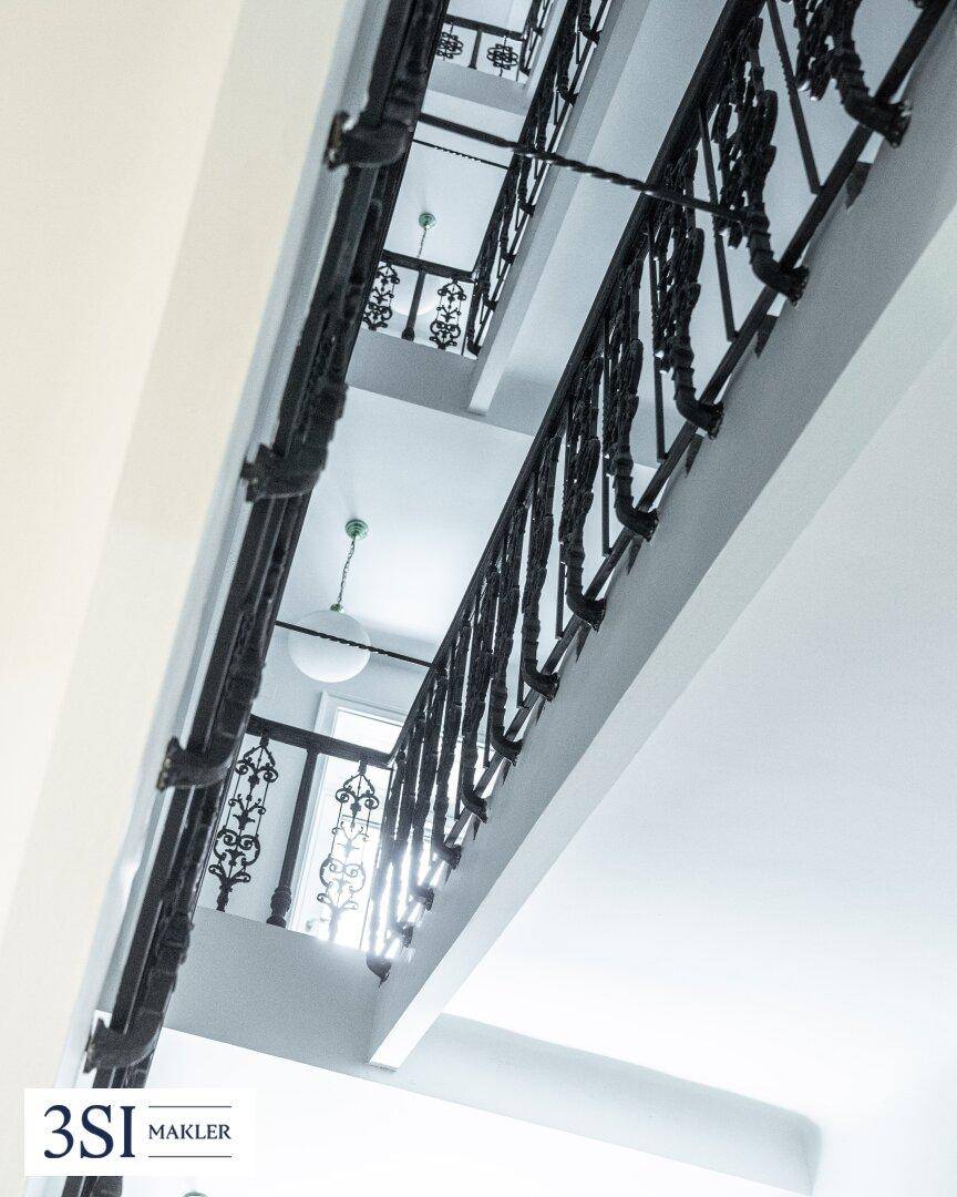 Elegantes Treppenhaus mit kunstvollen schwarzen Geländern und viel Tageslicht.